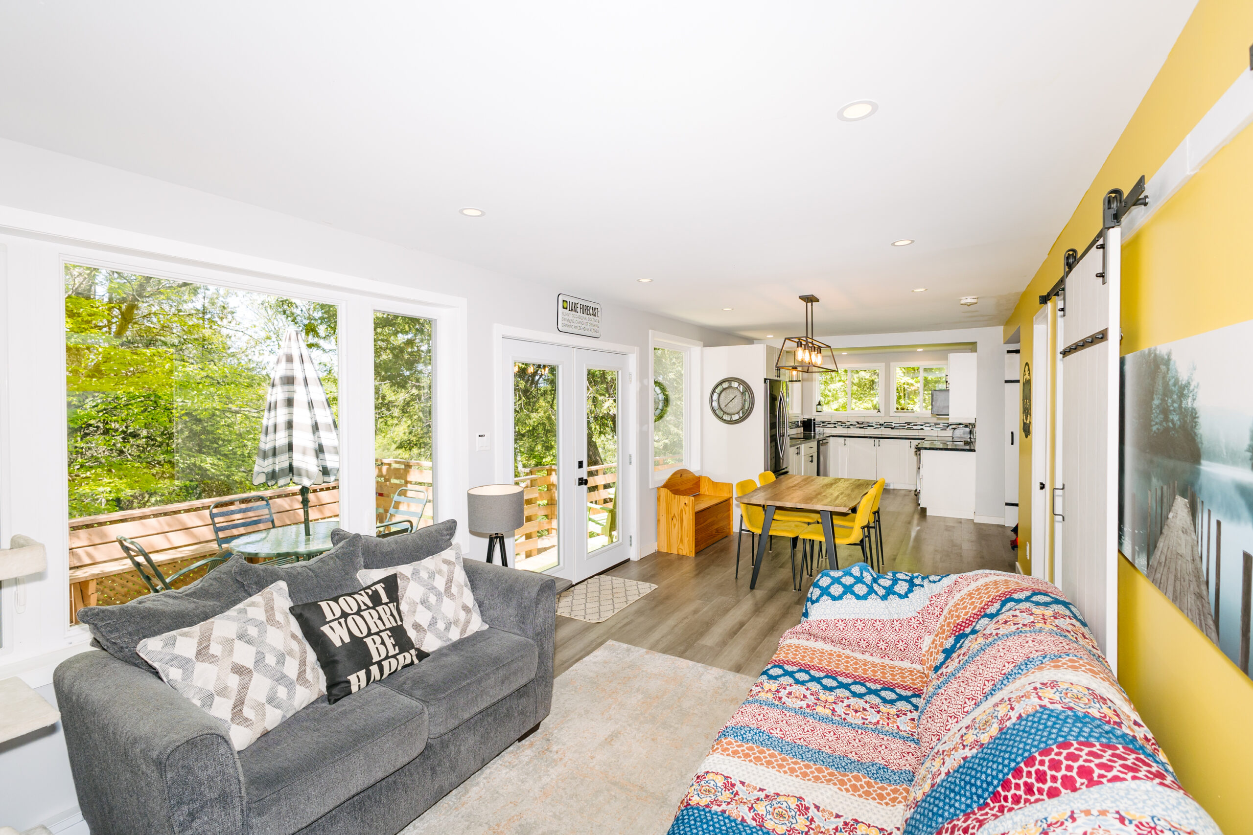Small grey couch against glass windows showing backyard trees faces a blue couch