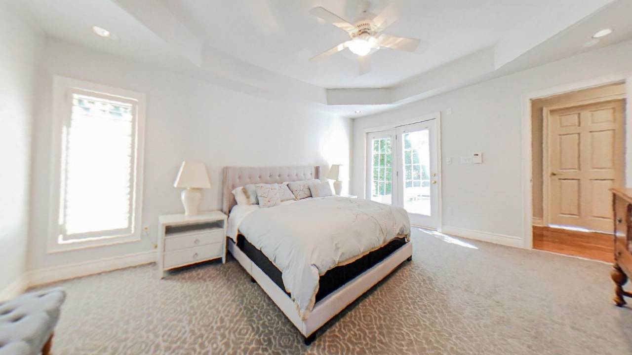 A large white room with an overhead fan. A white bed with white side tables on a white carpet