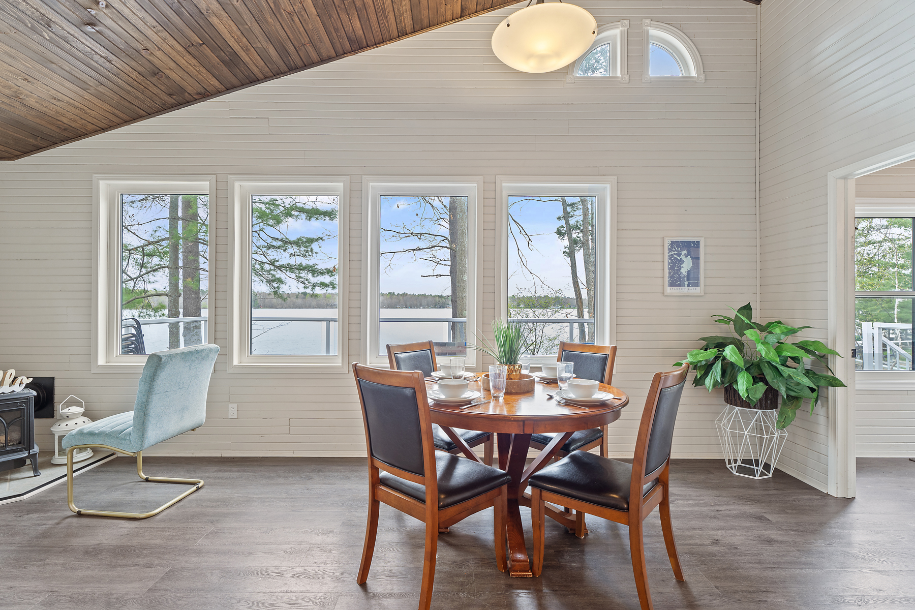 A dining area in front of big windows. A slanted wood-paneled ceiling slopes overhead.