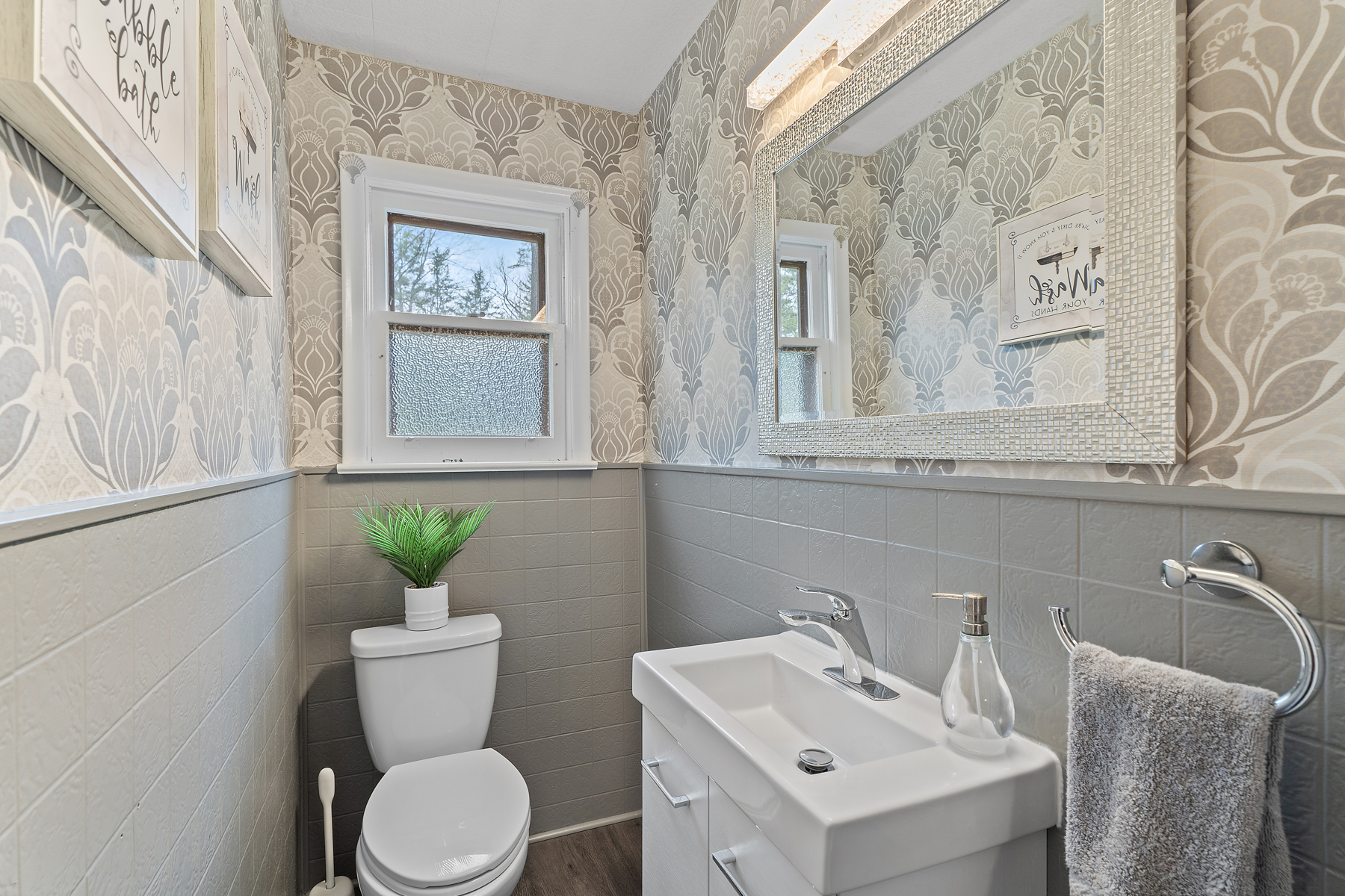 A small bathroom with a toilet, a sink, and neutral-coloured floral wallpaper.