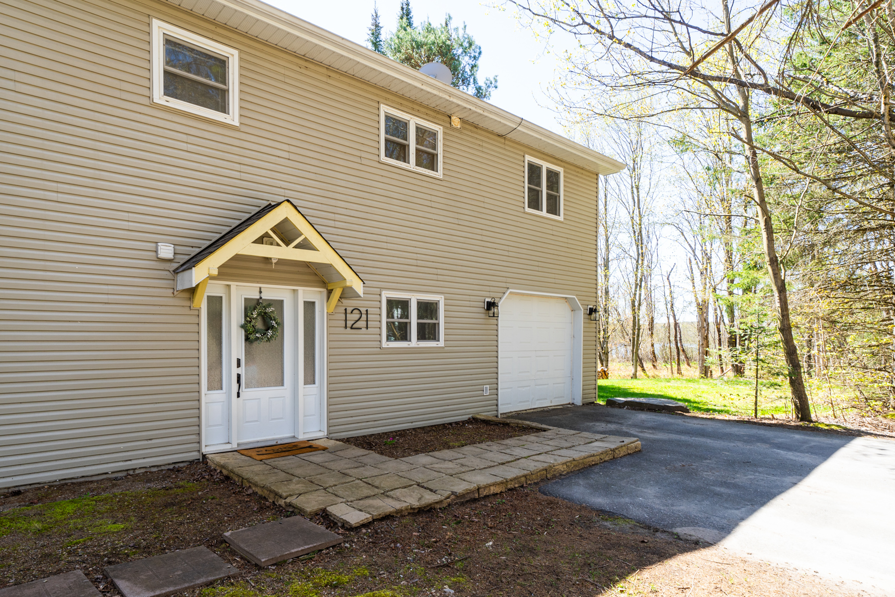 Entrance to a light brown panelled cottage with a driveway and small windows