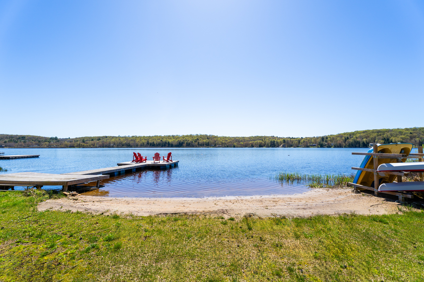 A small sandy beach meets the edge of the grassy backyard and blue lake