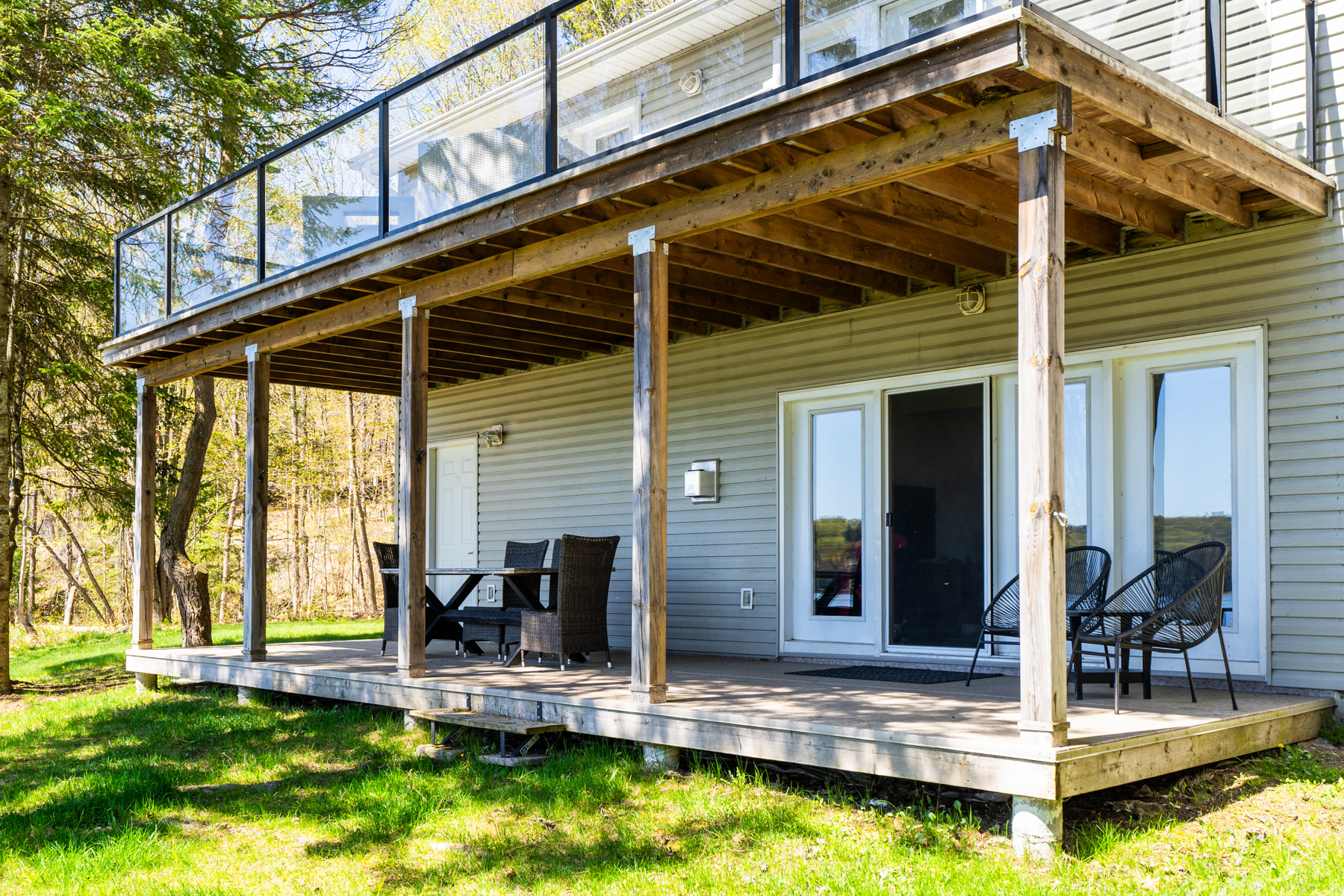 A two-level deck. On the lower level, a dining table and doors to the inside. The top has glass railings
