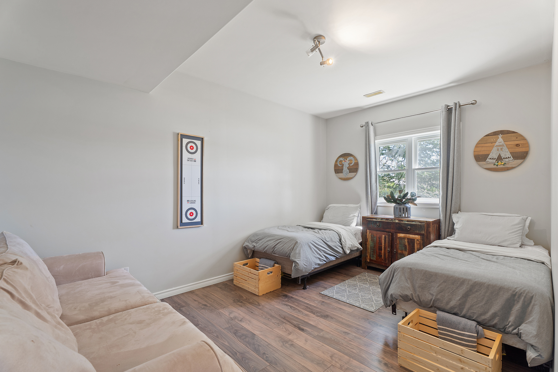Two twin beds with grey covers sit against a wall with bright window