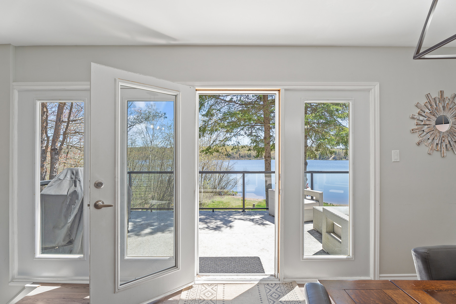 Glass doors with a white frame open to a bright upper-level deck with the lake in the distance