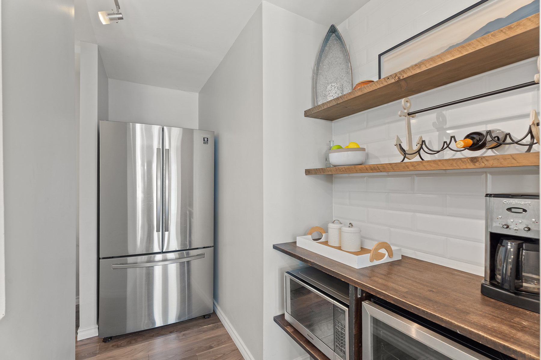 Stainless steel fridge sits in the corner of the kitchen next to wooden shelves