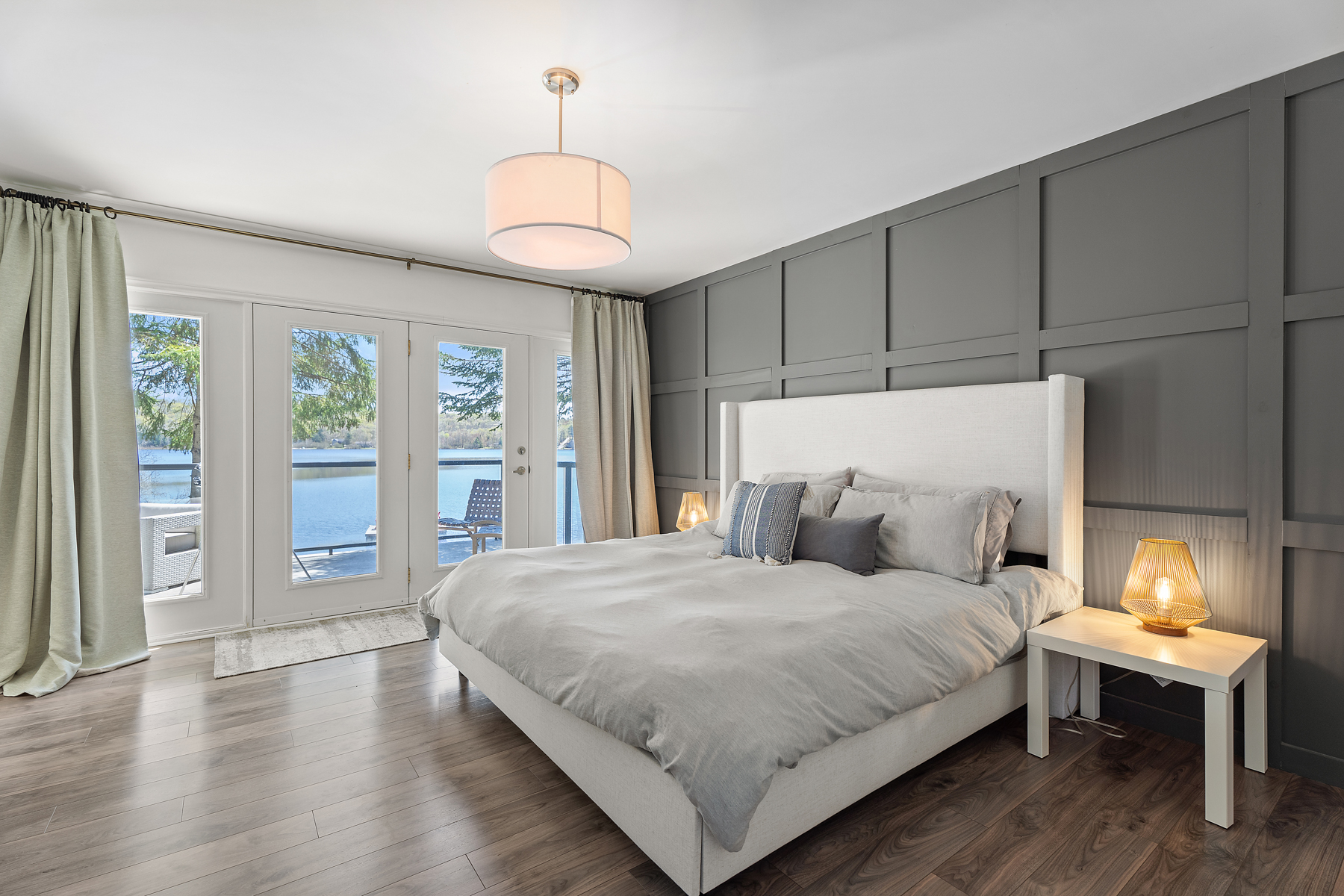 The white bed faces a brown dresser and is next to bright windows that step out onto the upper deck