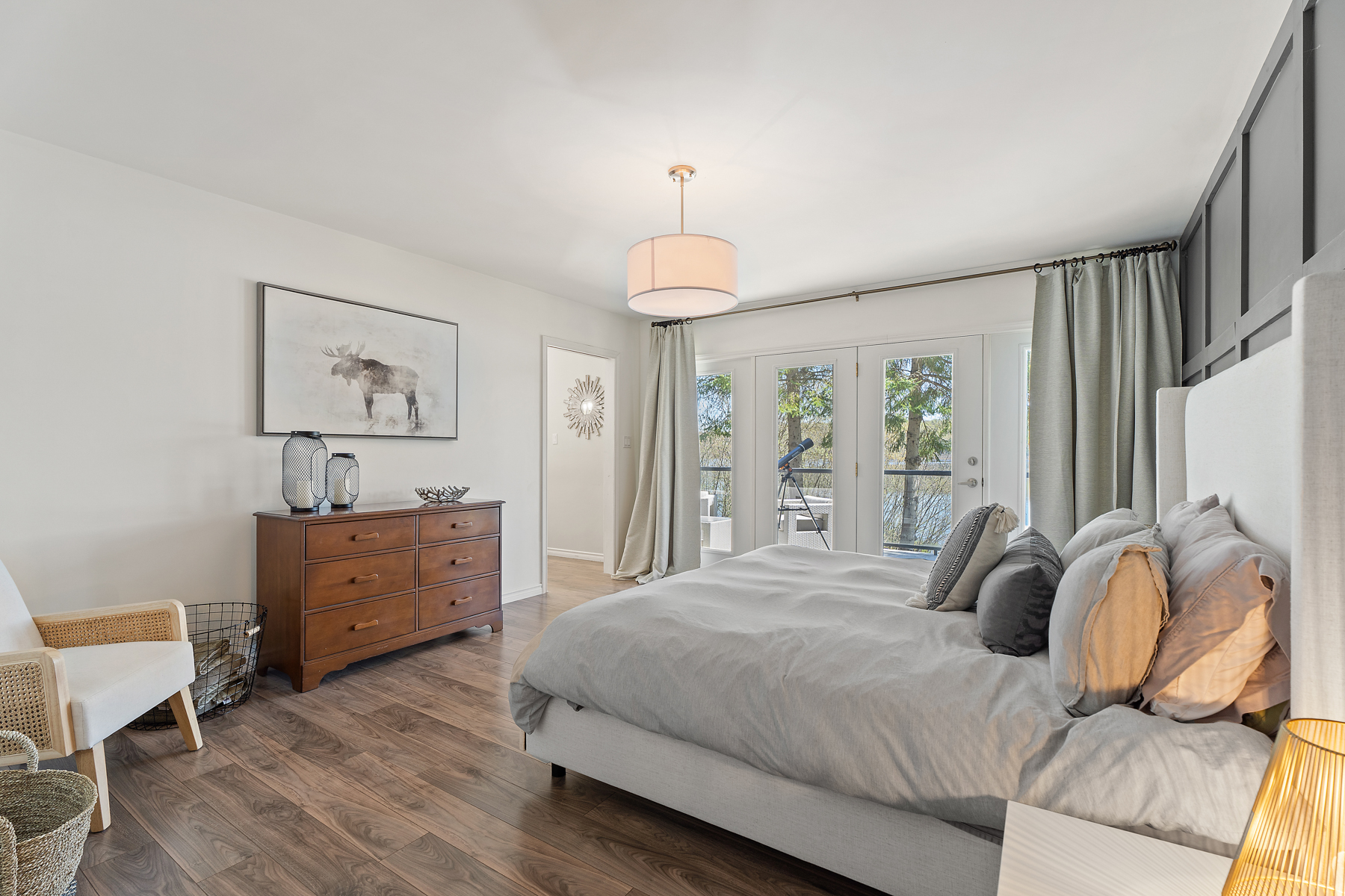 The white bed faces a brown dresser and is next to bright windows that step out onto the upper deck