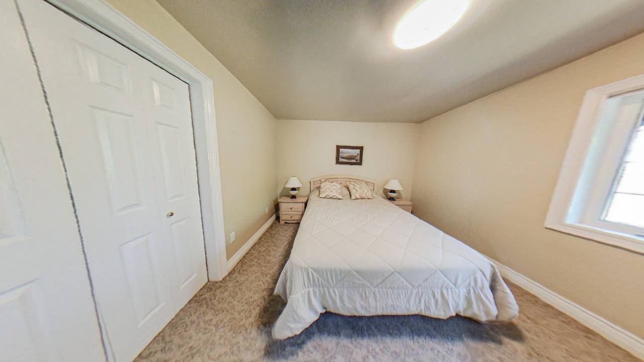A white bed fits inside a bare white room next to a closet