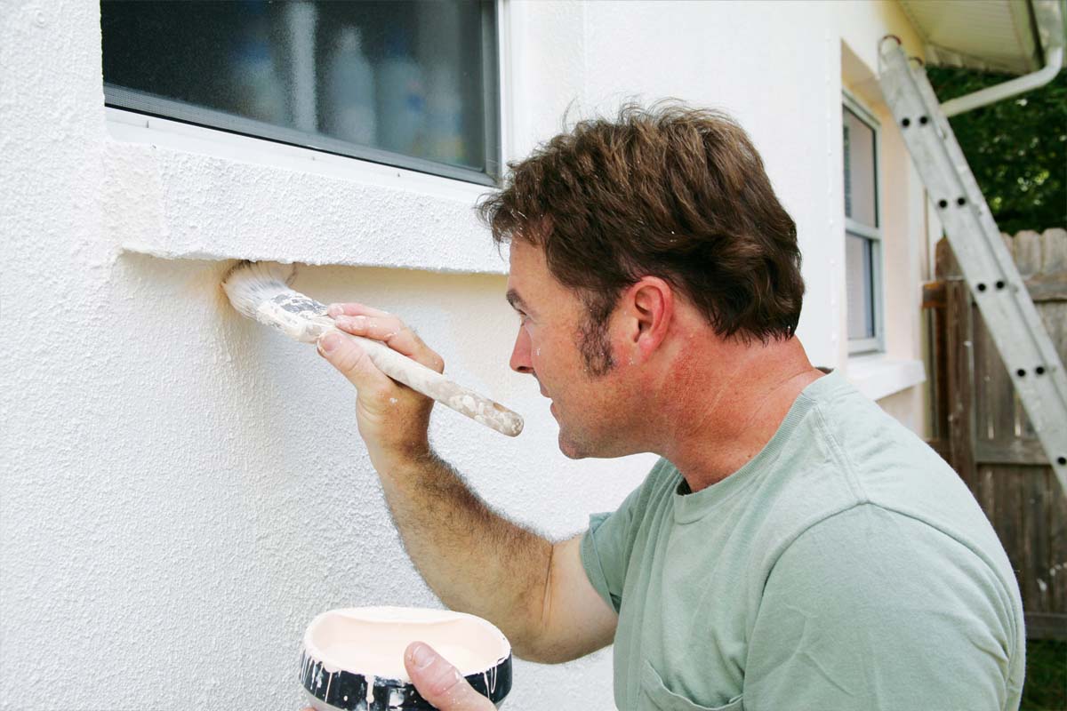 a caucasian man painting the exterior of a house