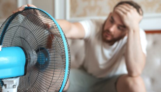 A bearded man sitting in front of an electric fan