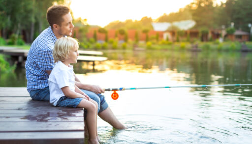 A man and child sitting at the end of a dock with a fishing rod