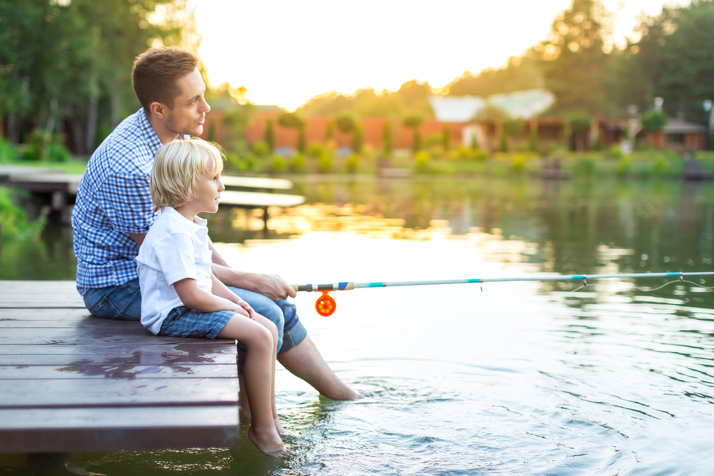 A man and child sitting at the end of a dock with a fishing rod