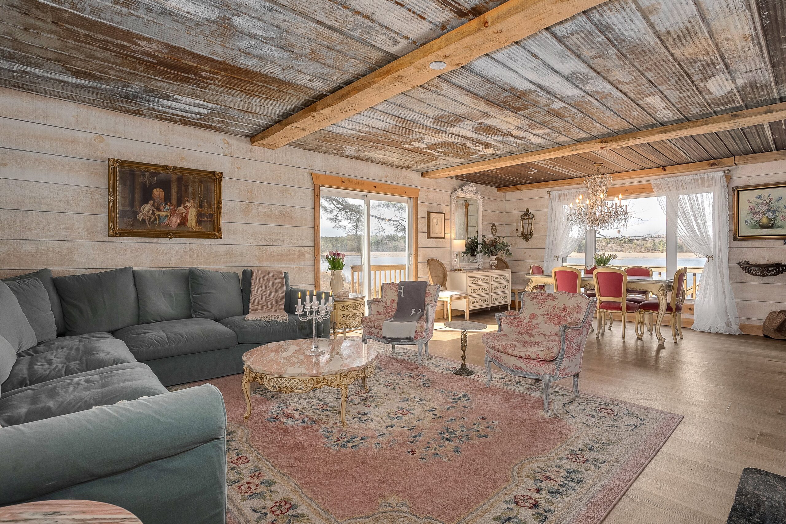 A turquoise velvet couch on a pink rug faces pink chairs and opens to the dining room