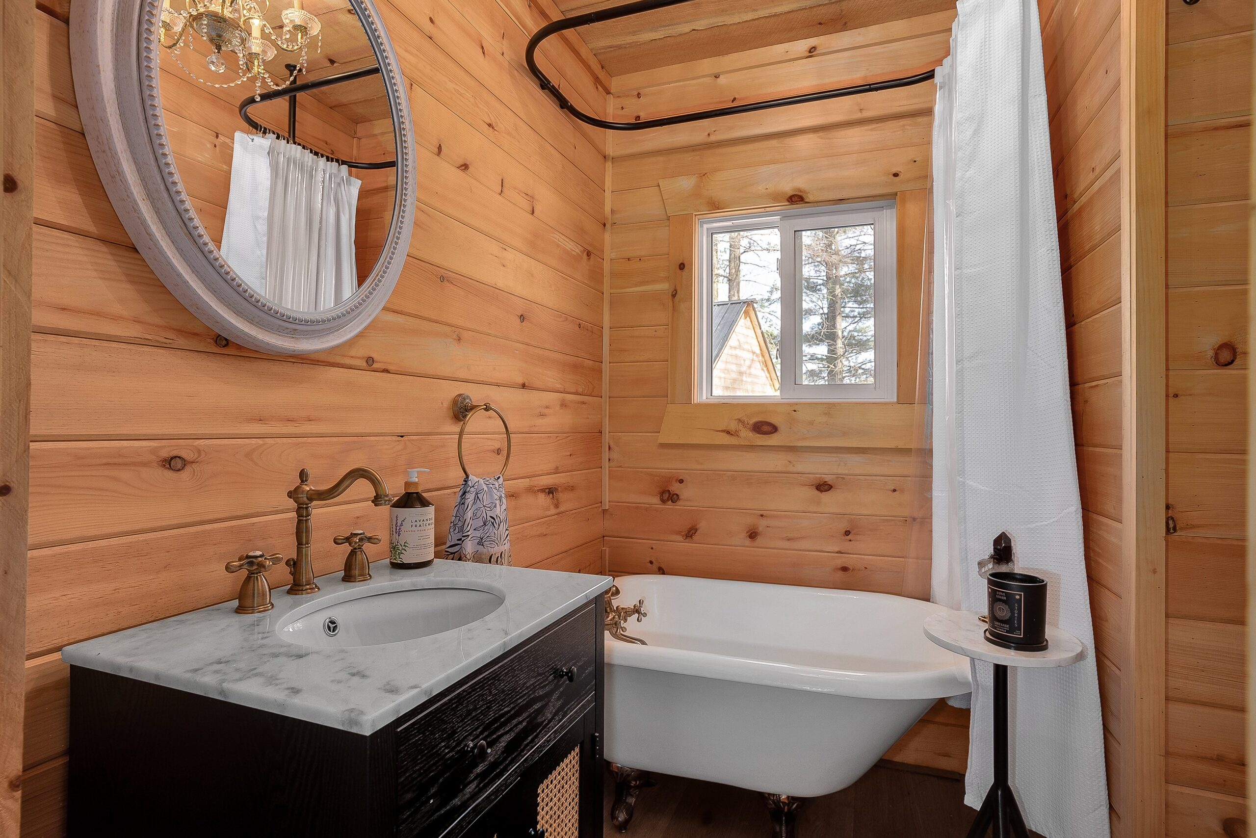A wood-panelled bathroom with a white tub, a black vanity and a mirror