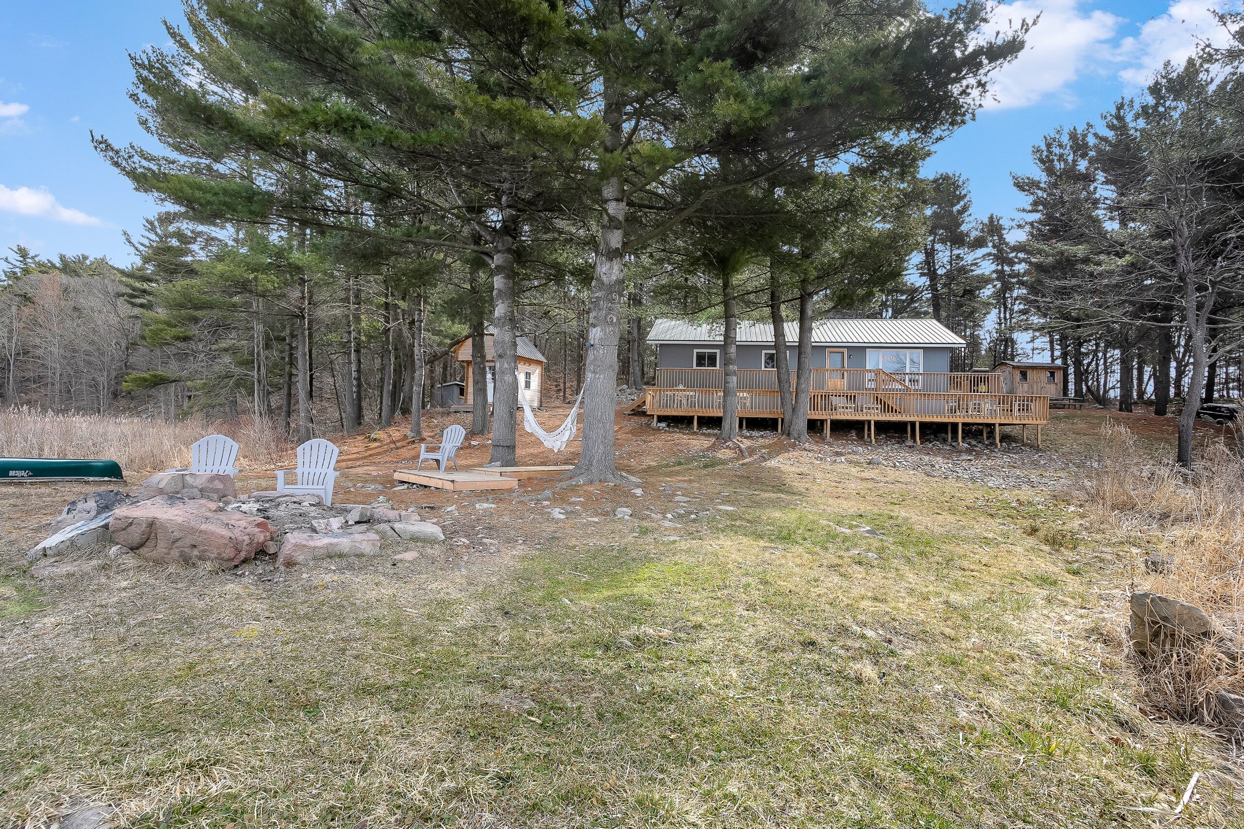 A fire pit with chairs around in an open yard with the grey cottage behind