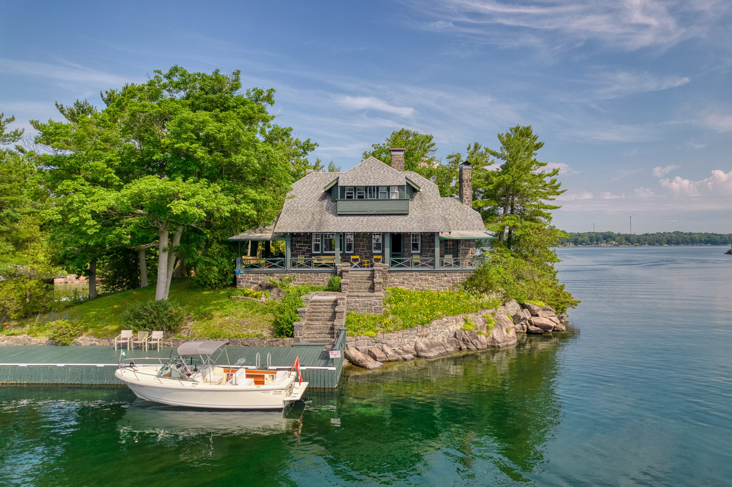 A stone cottage with green trim on a green island. In front of the island, a green dock with a white parked boat