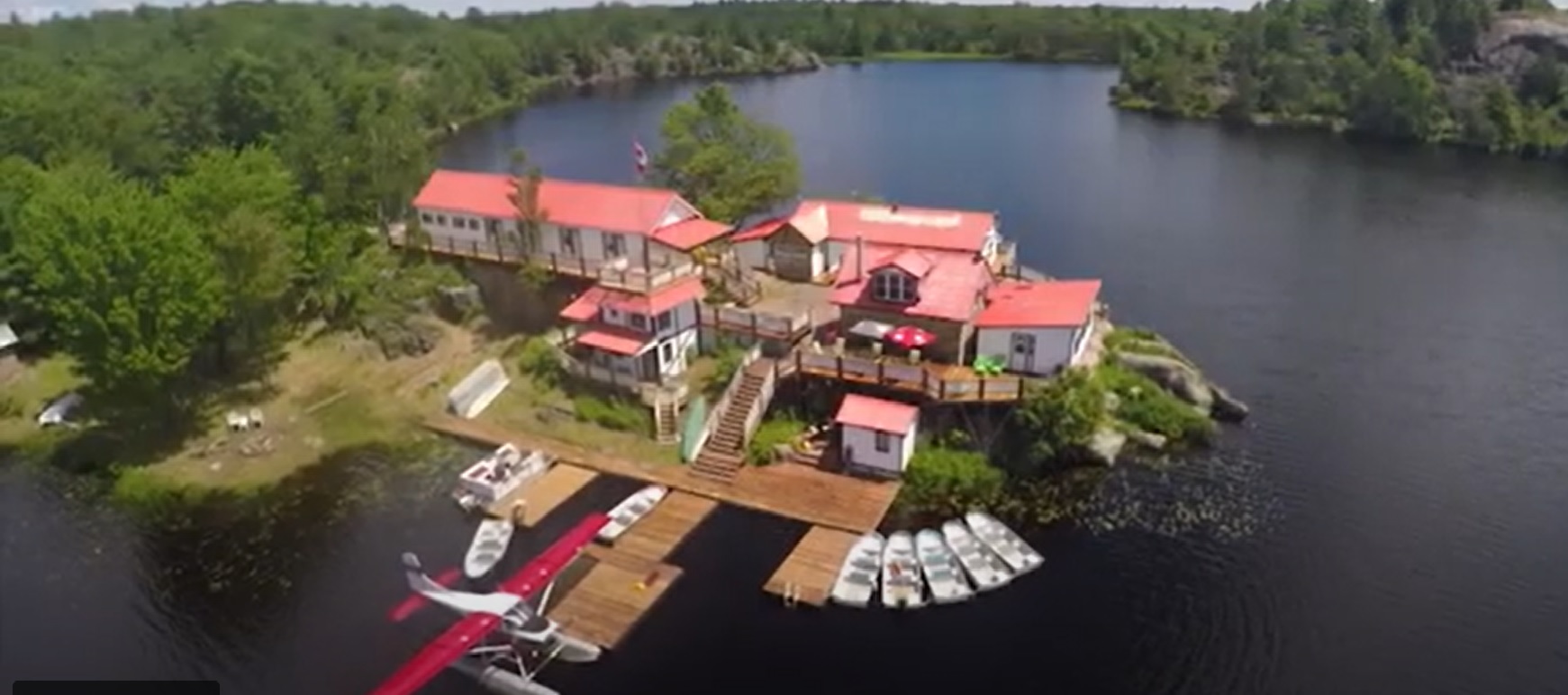 A sprawling white lodge with a red roof is surrounded by a lake.