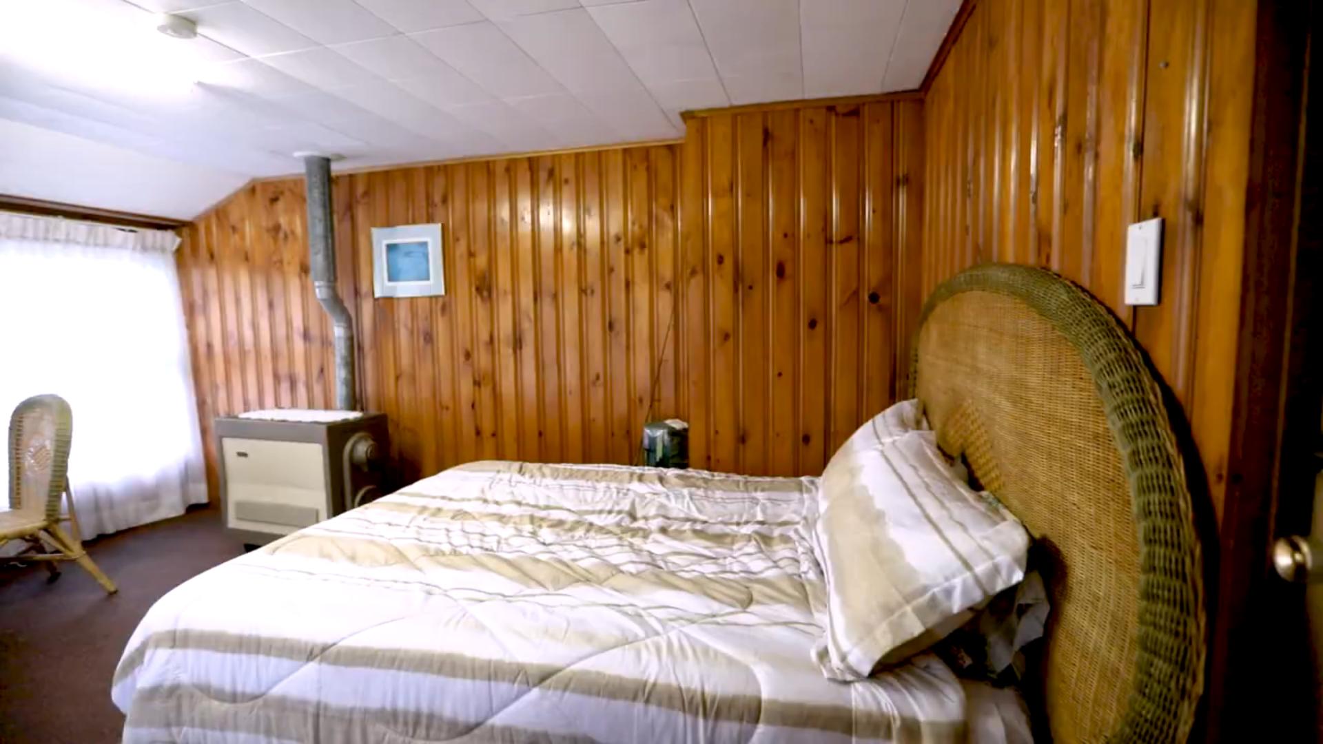 A bed is pressed against a brown wood panelled wall