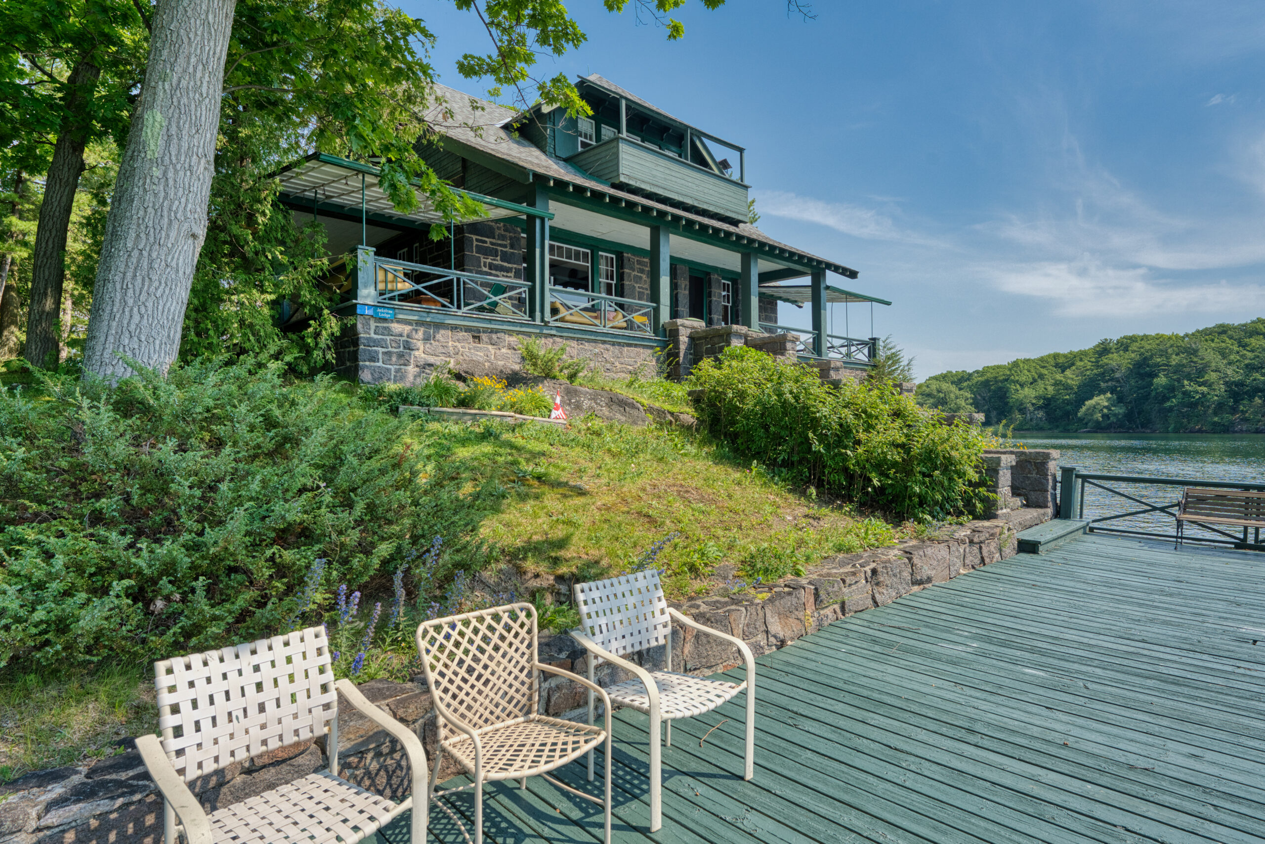 Three patio chairs on a green dock with the stone cottage behind