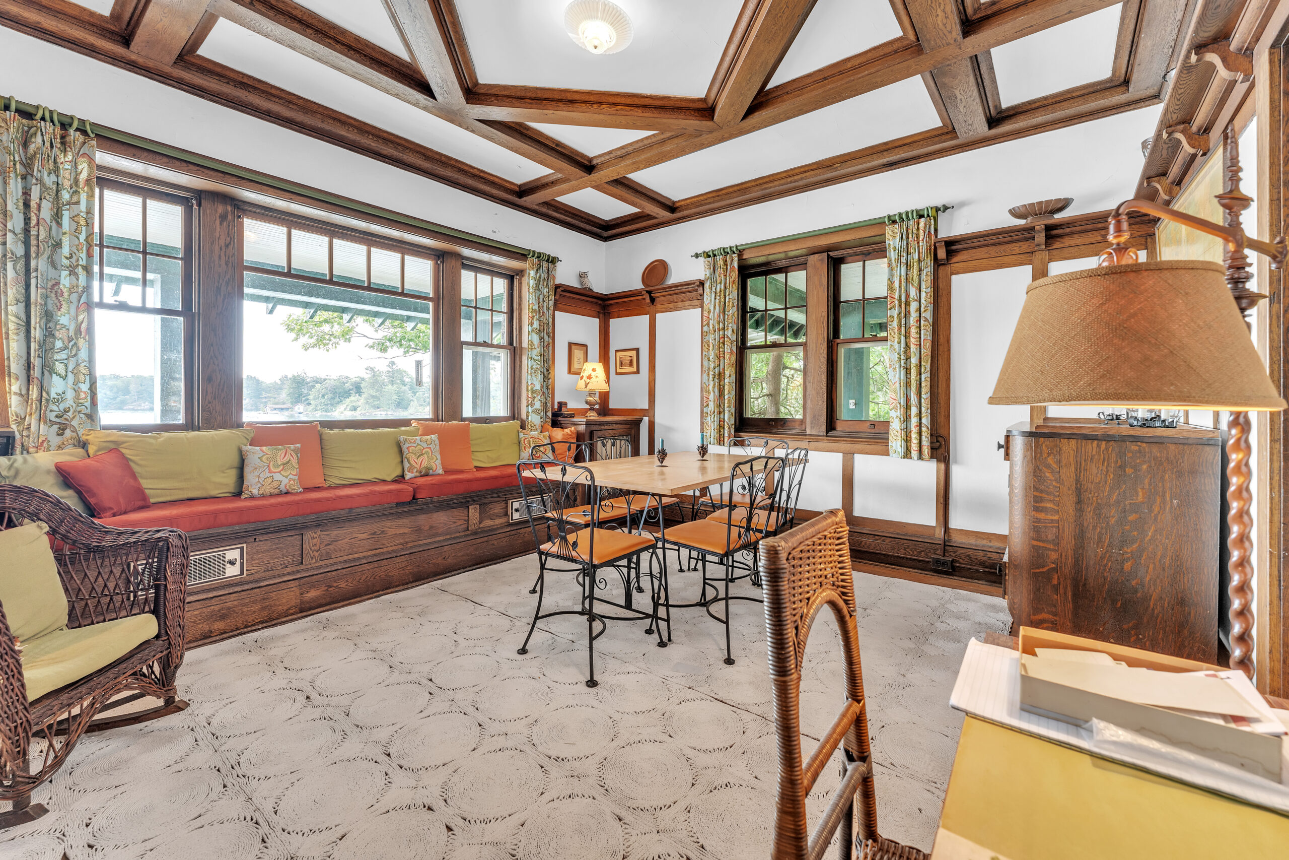 In a room with tall ceilings, a wood dining table sits in the centre of the room. A window sitting area sits along the back of the room