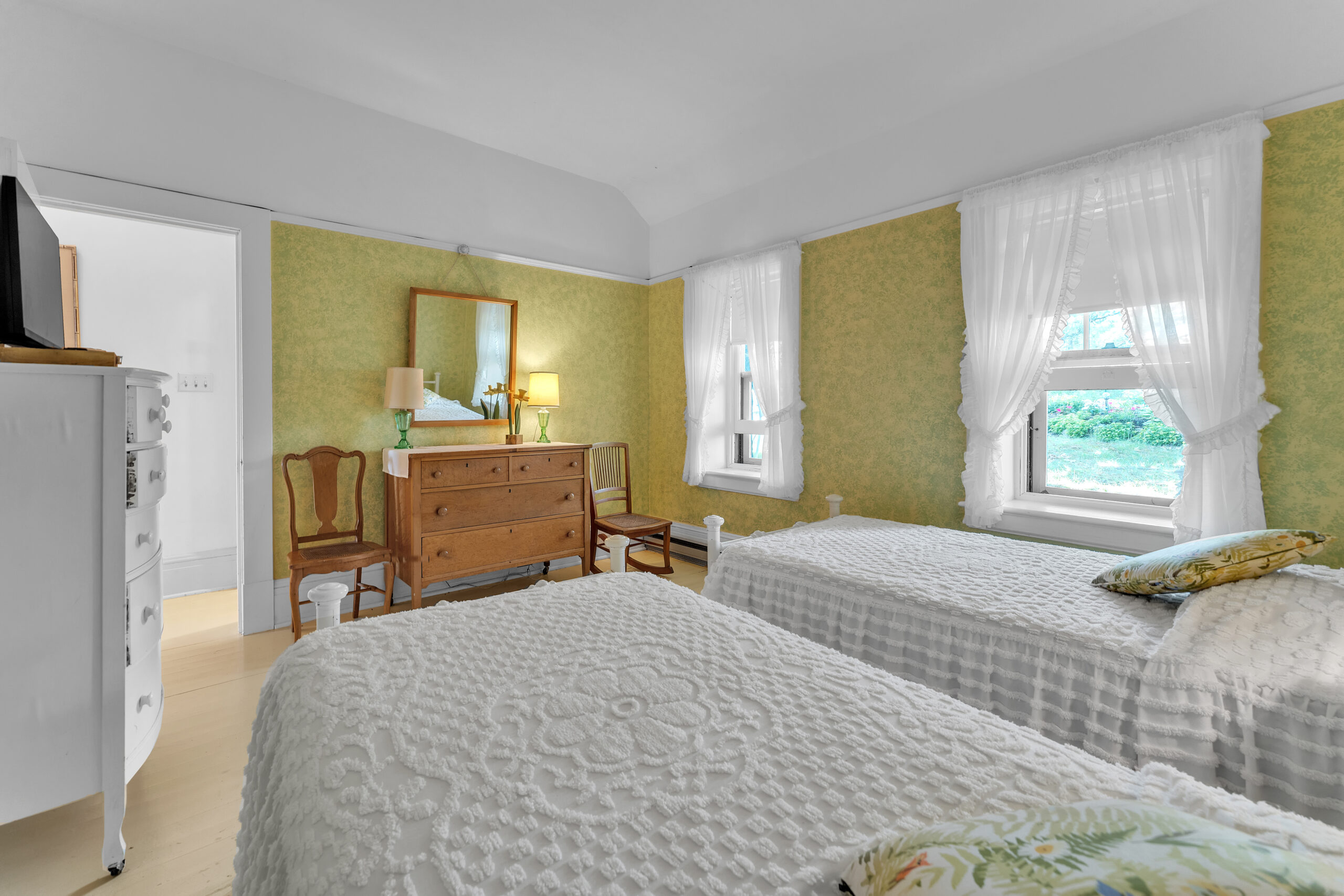 Two white beds face a wood dresser and mirror in a green bedroom