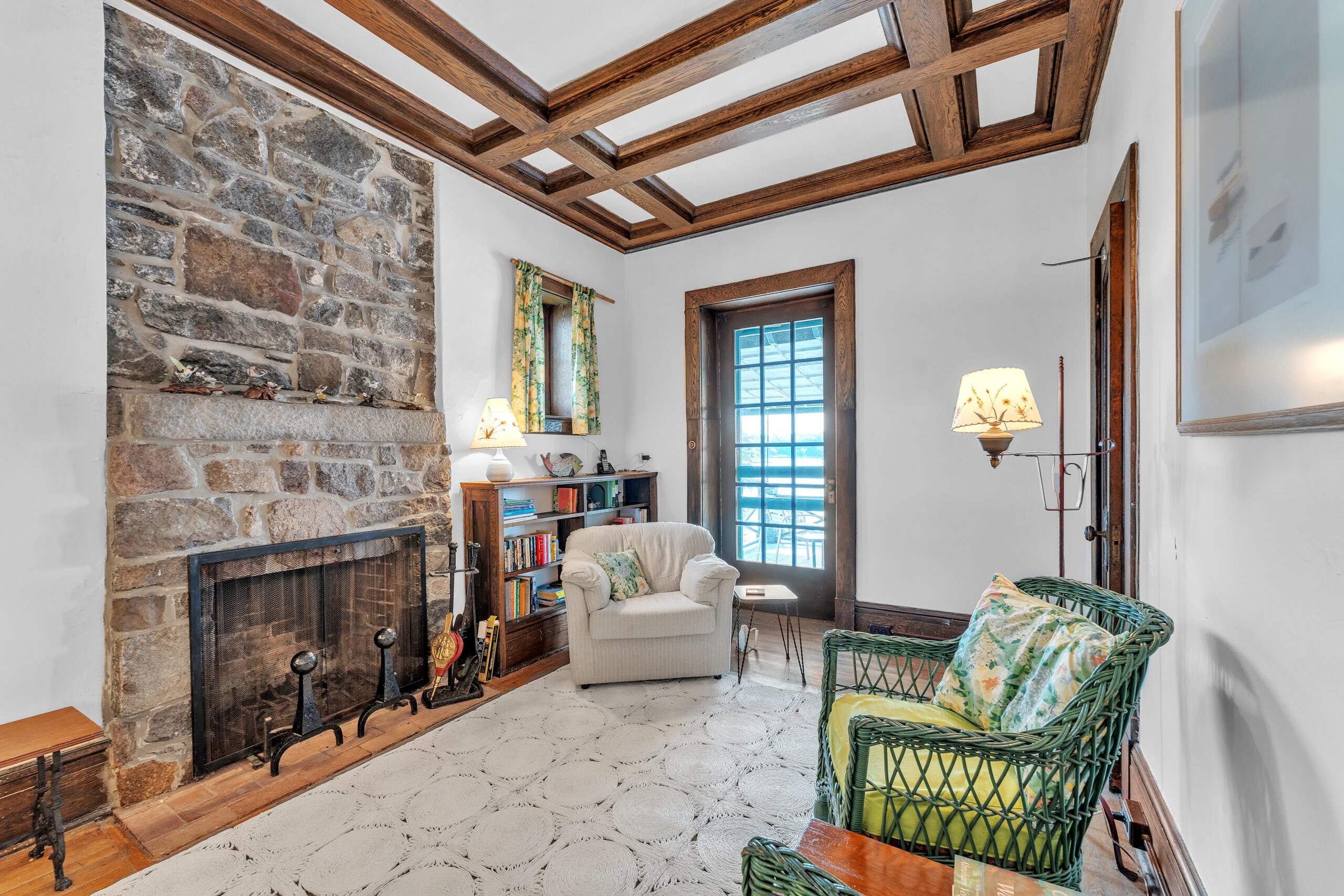A white chair perpendicular to two green wicker chairs and a large stone fireplace