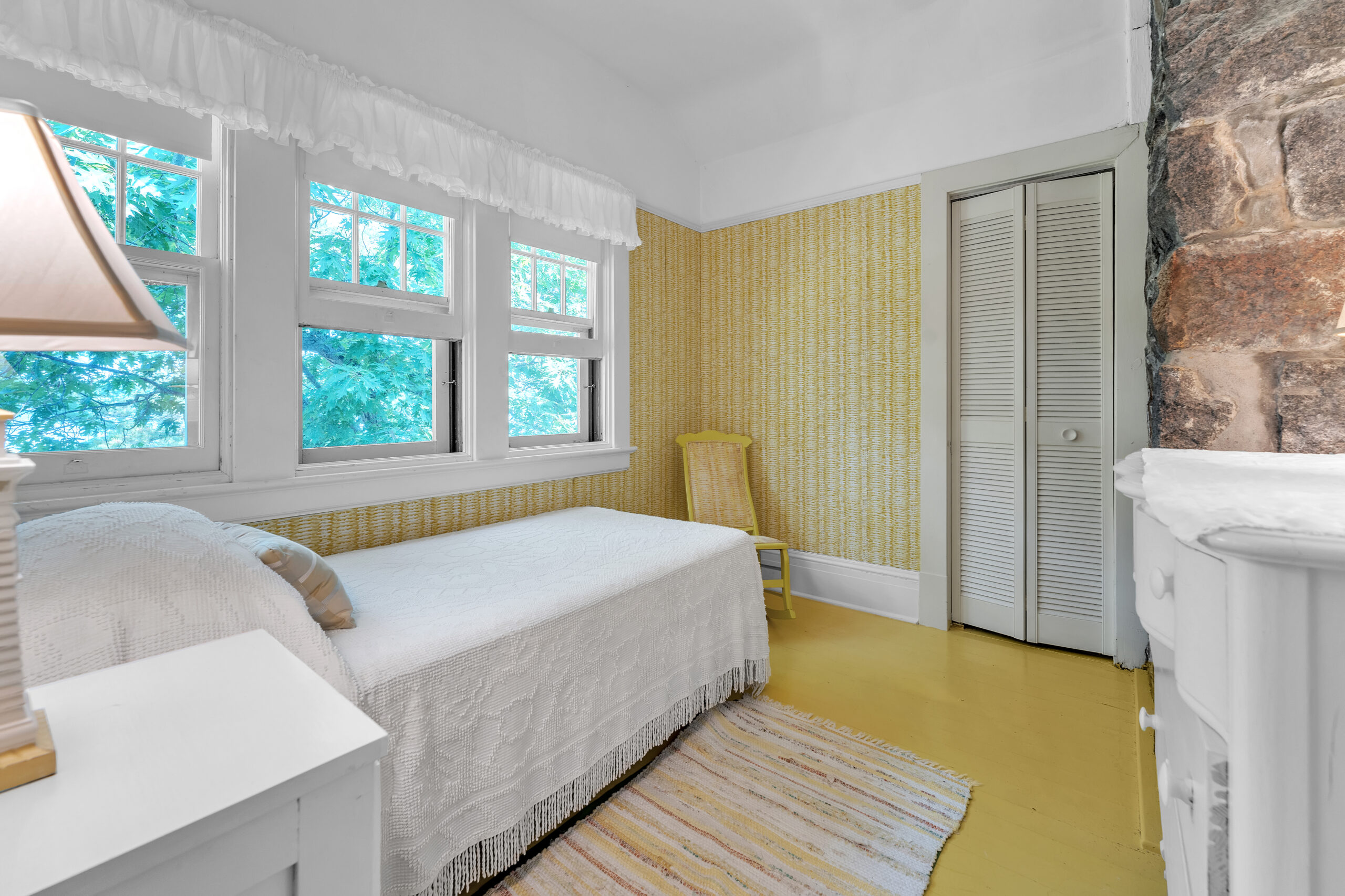 Reverse view of the white twin bed in a yellow room
