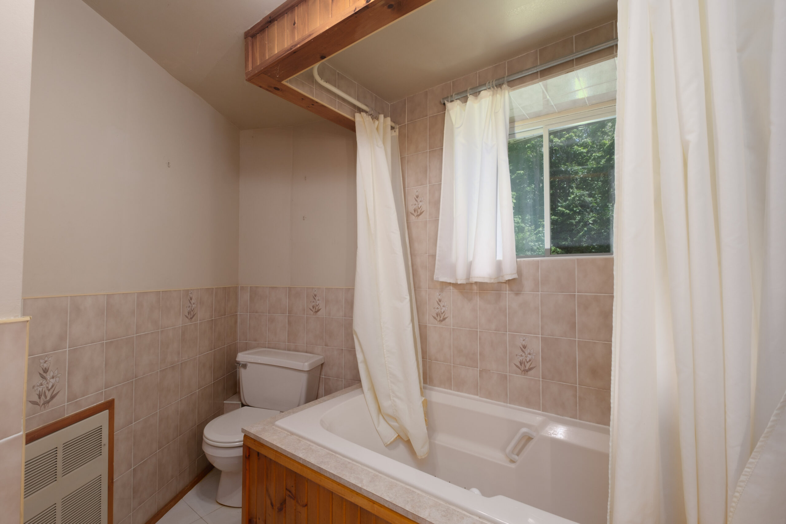 A small white toilet next to a wood-lined bathtub with an open shower curtain