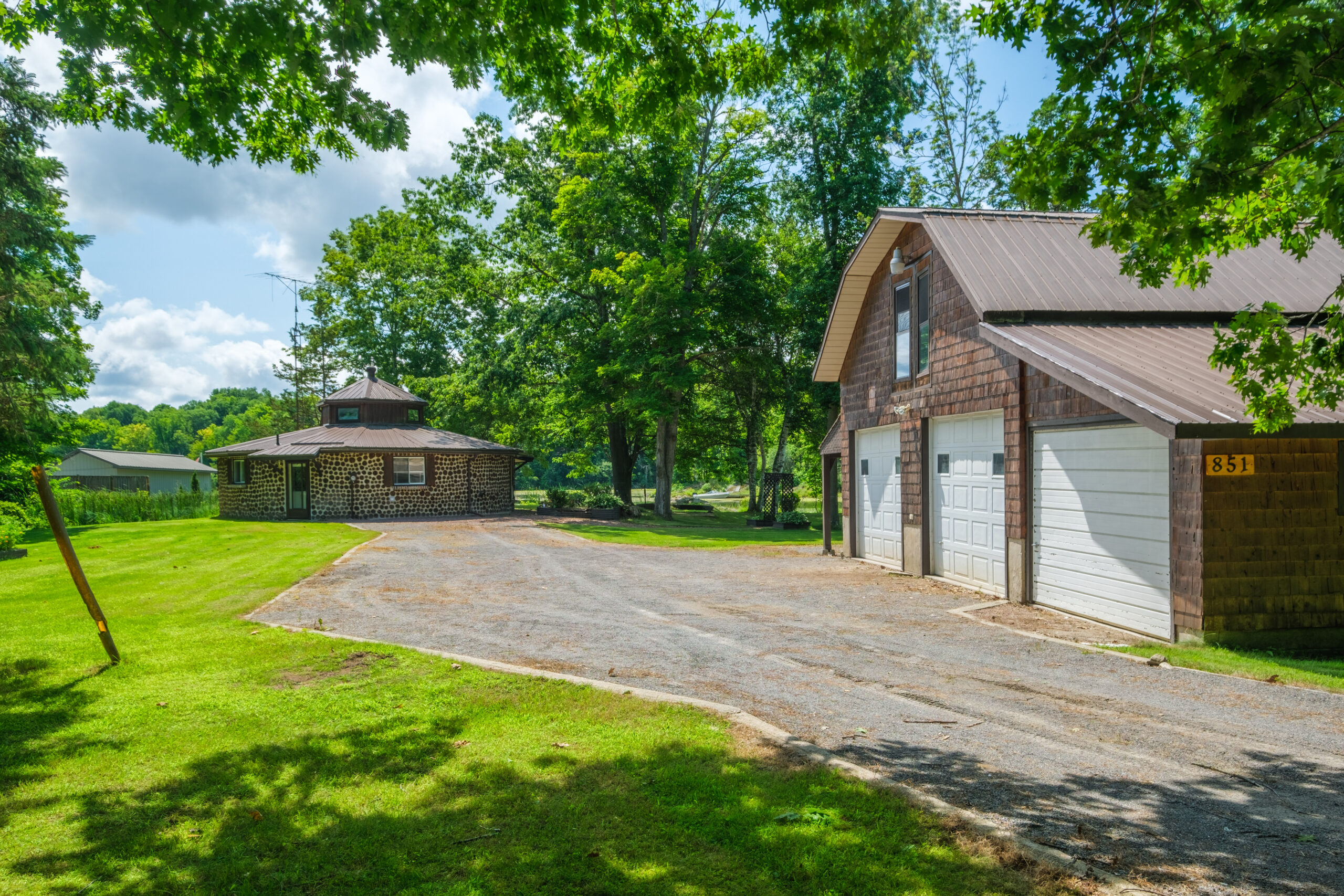 A large garage sits on the right of a long driveway. At the end of the driveway, a round stone house