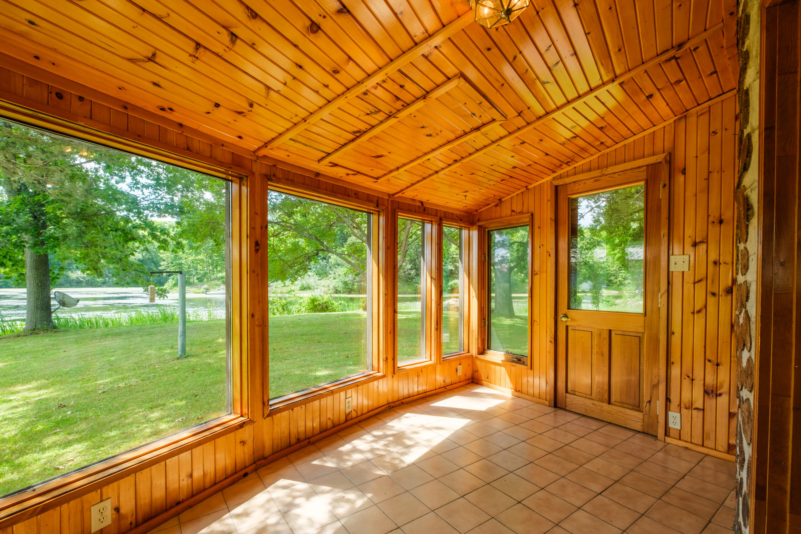 A wood panelled sunroom with floor-to-ceiling windows and tiled floors