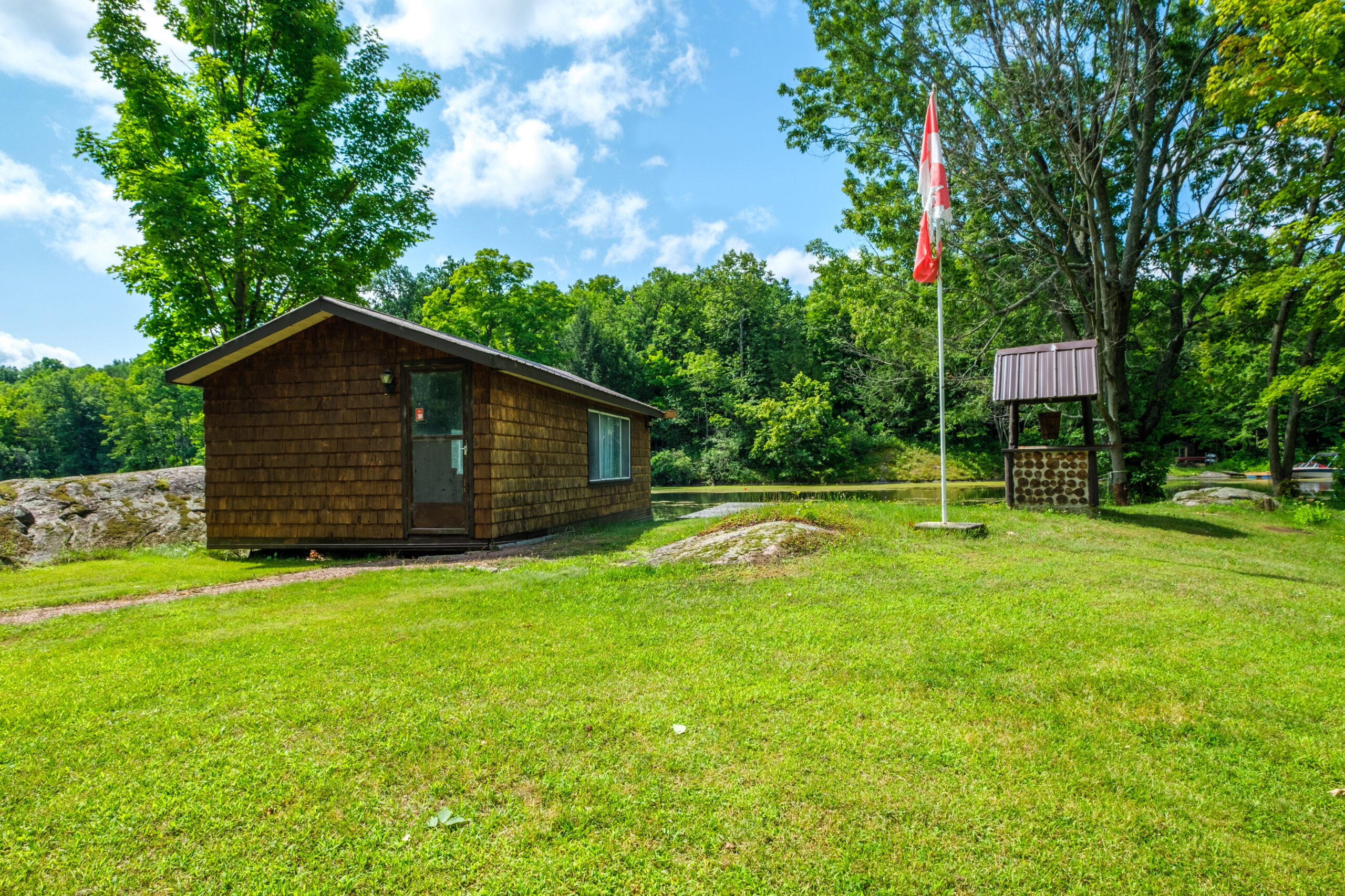 A small dark brown wood building in a grassy area next to a flagpole with a Canada Flag