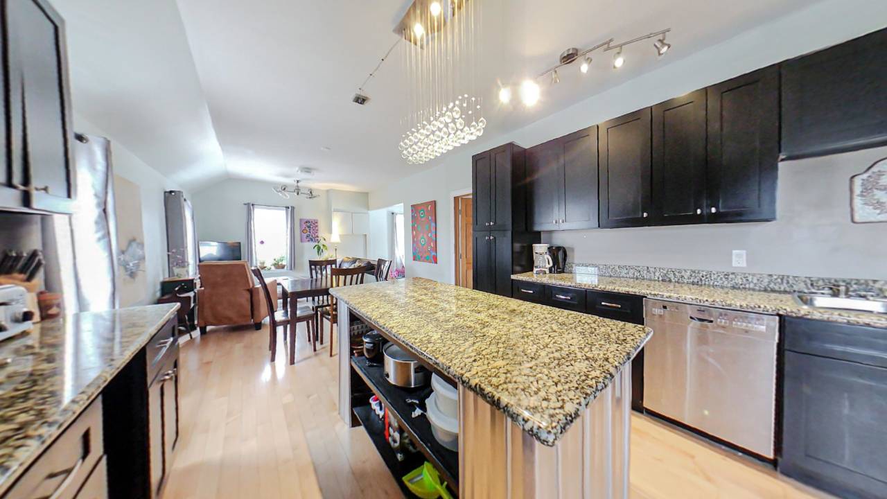 A kitchen island next to brown kitchen cabinets. Behind, a family room