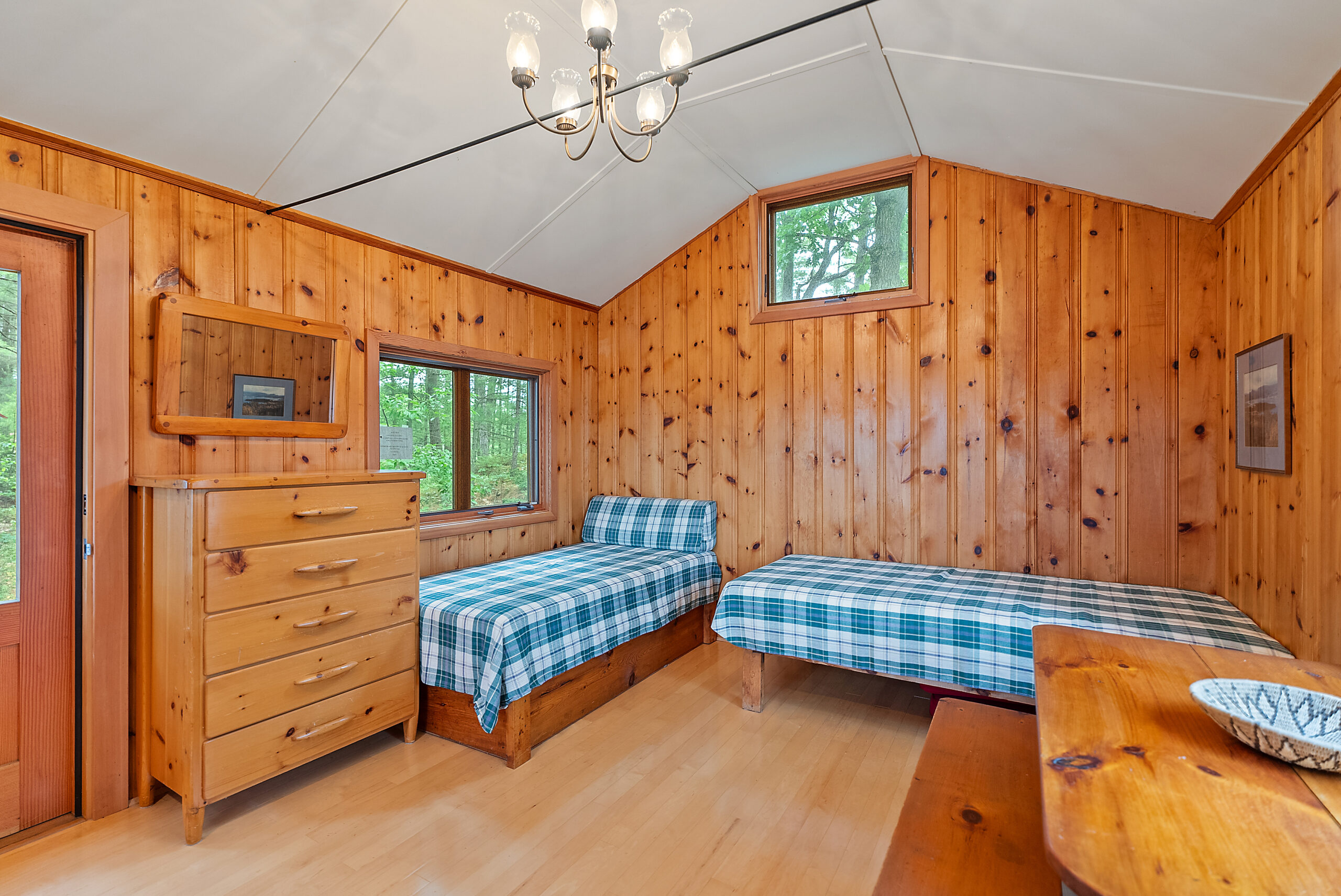 Two twin beds with blue plaid covers are in an L-shape in a red wood room