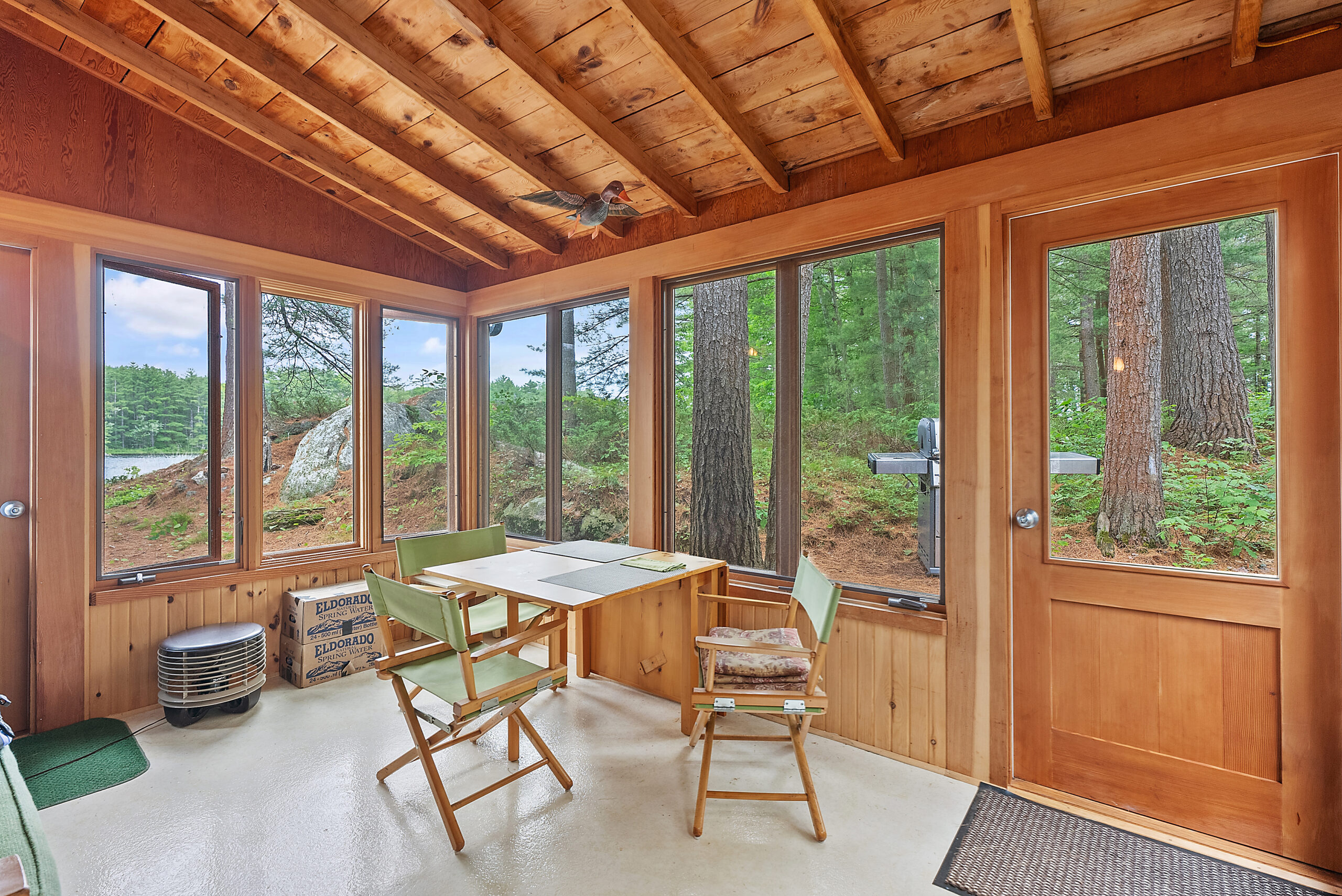 A rustic wood sunroom with vaulted ceilings looks out to the lake
