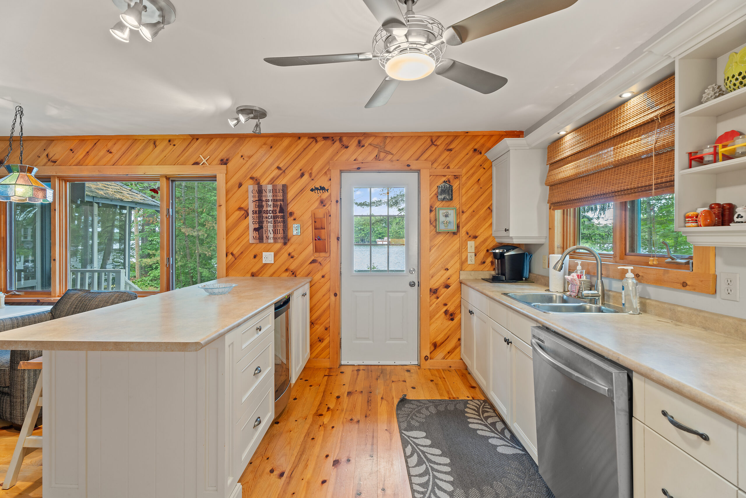 A white kitchen island across from white cabinets and a stainless steel dishwasher. Between them is a white door set into wood walls