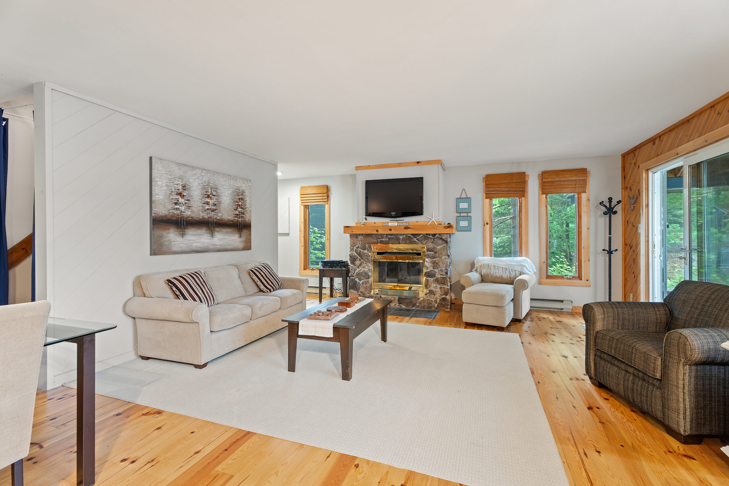 A large stone fireplace in the middle. To the left, a white couch facing a small coffee table on a white carpet faces a large window