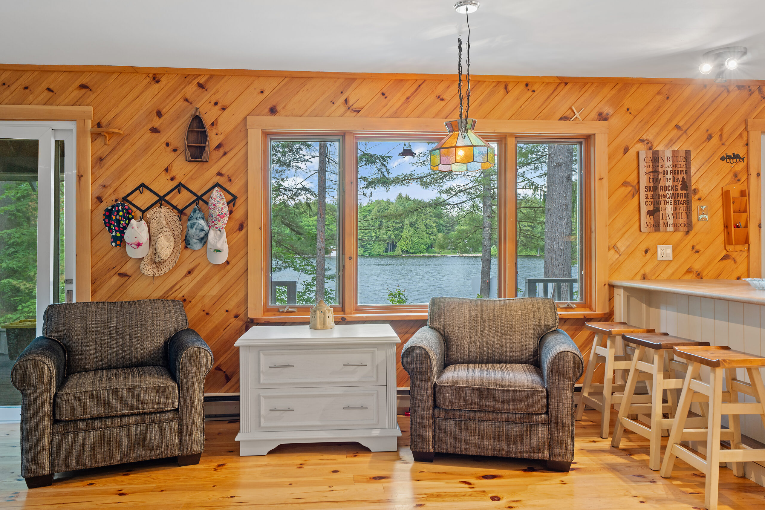 Two brown love seats on the back of the wood-panelled wall, with a large window facing the lake. A small white table between the chairs