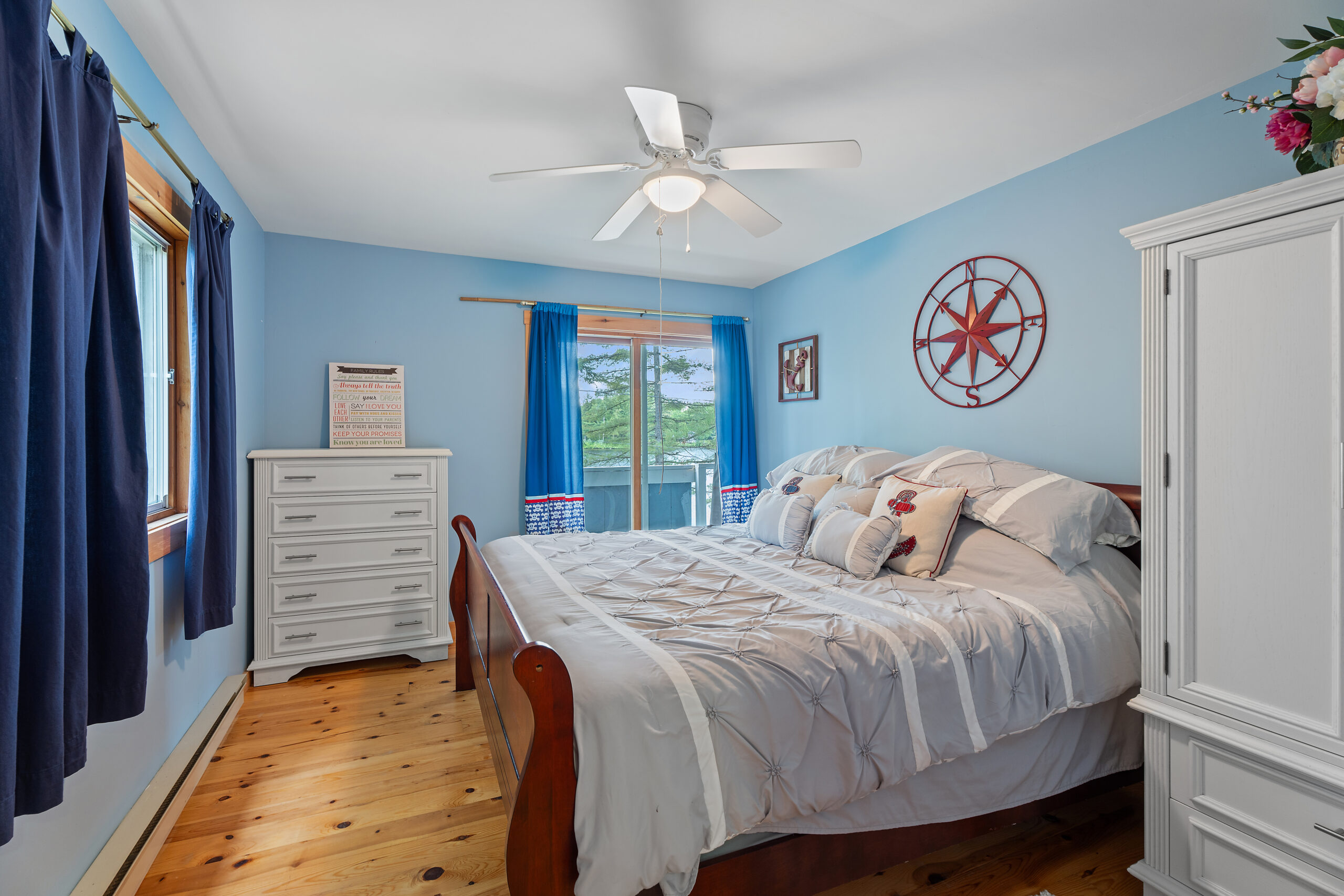 A blue stripped bed faces a window with blue curtains in a light blue room