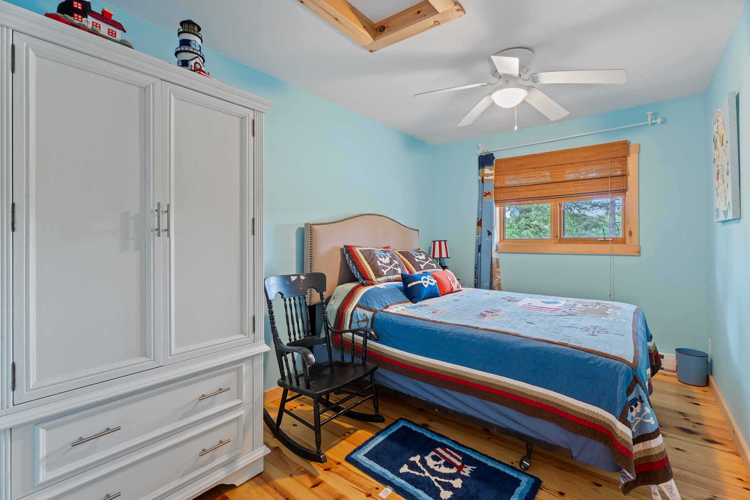 A blue and red stripped bed beside a large white wardrobe in a blue room