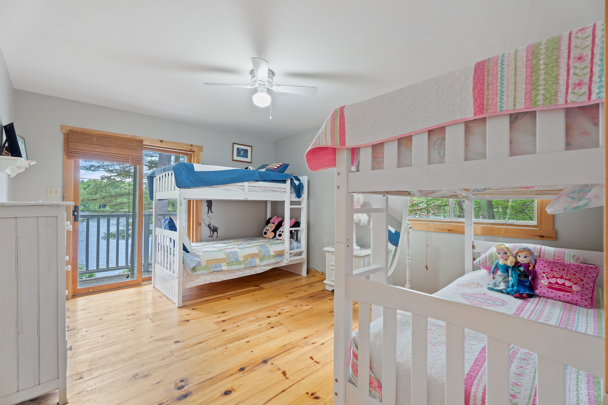 Two sets of white bunk beds in a white room. To the left, a glass door that faces the lake
