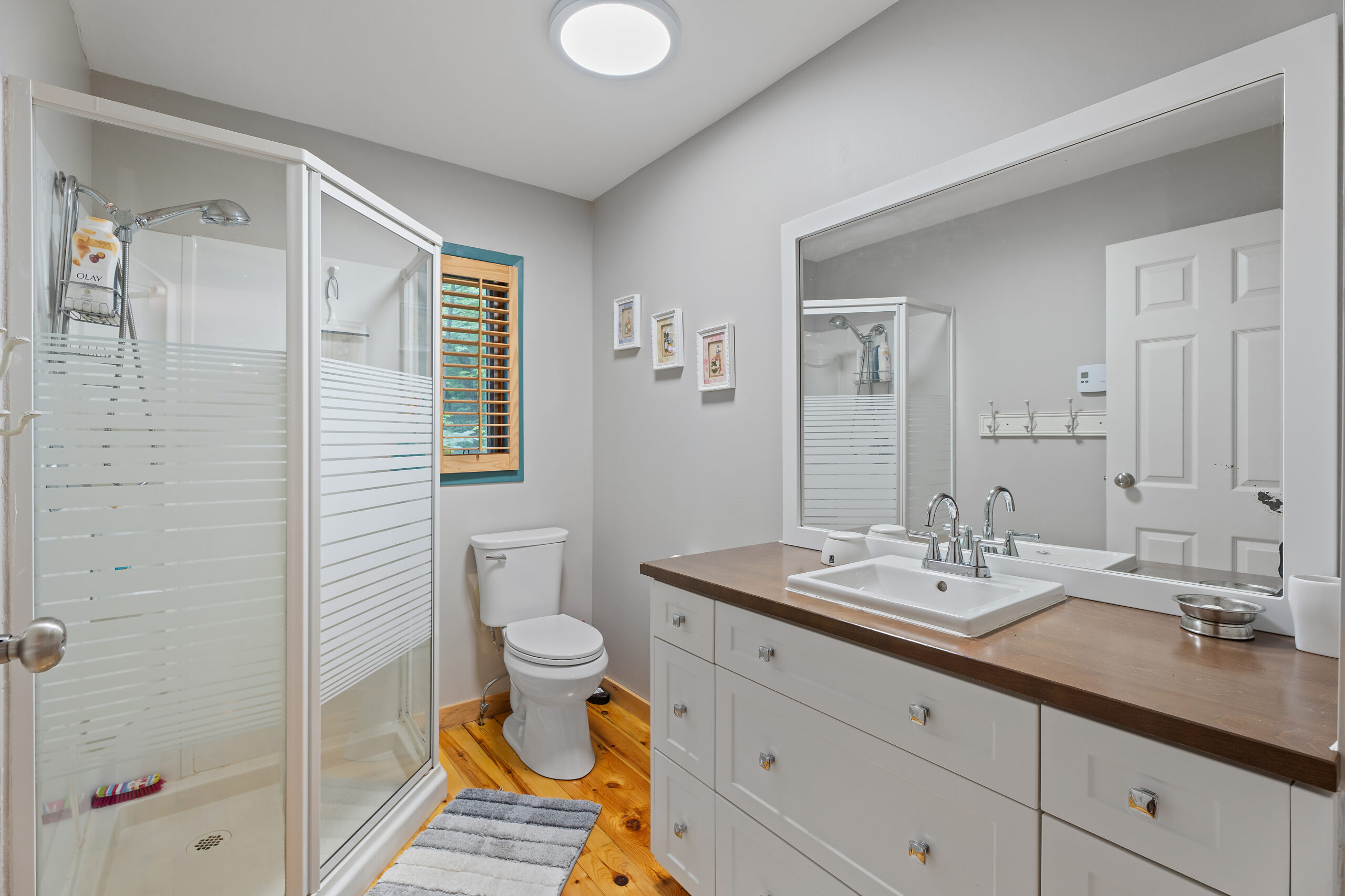 A white bathroom with a glass shower, white toilet, and vanity