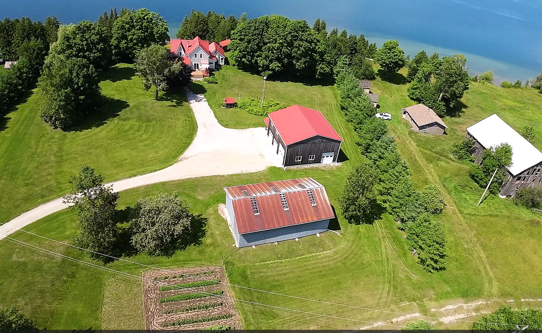 Aerial view of a large grassy property with three red-roofed building scattered around. A blue lake sits on the north edge