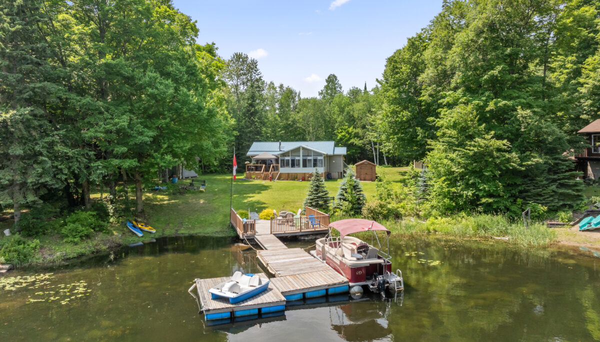 A bungalow cottage on a grassy lawn. In front, a large dock with a boat on each side