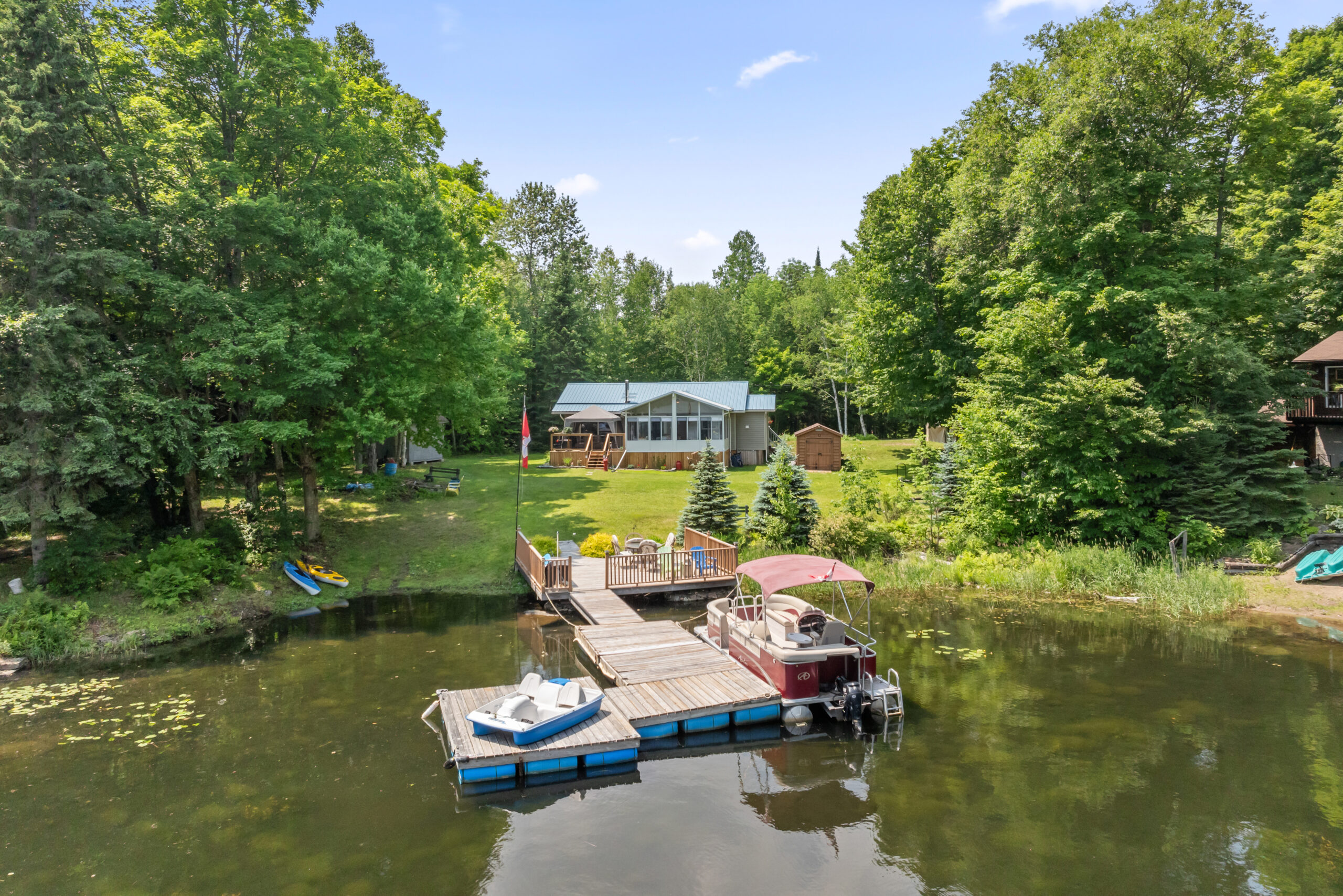 A bungalow cottage on a grassy lawn. In front, a large dock with a boat on each side