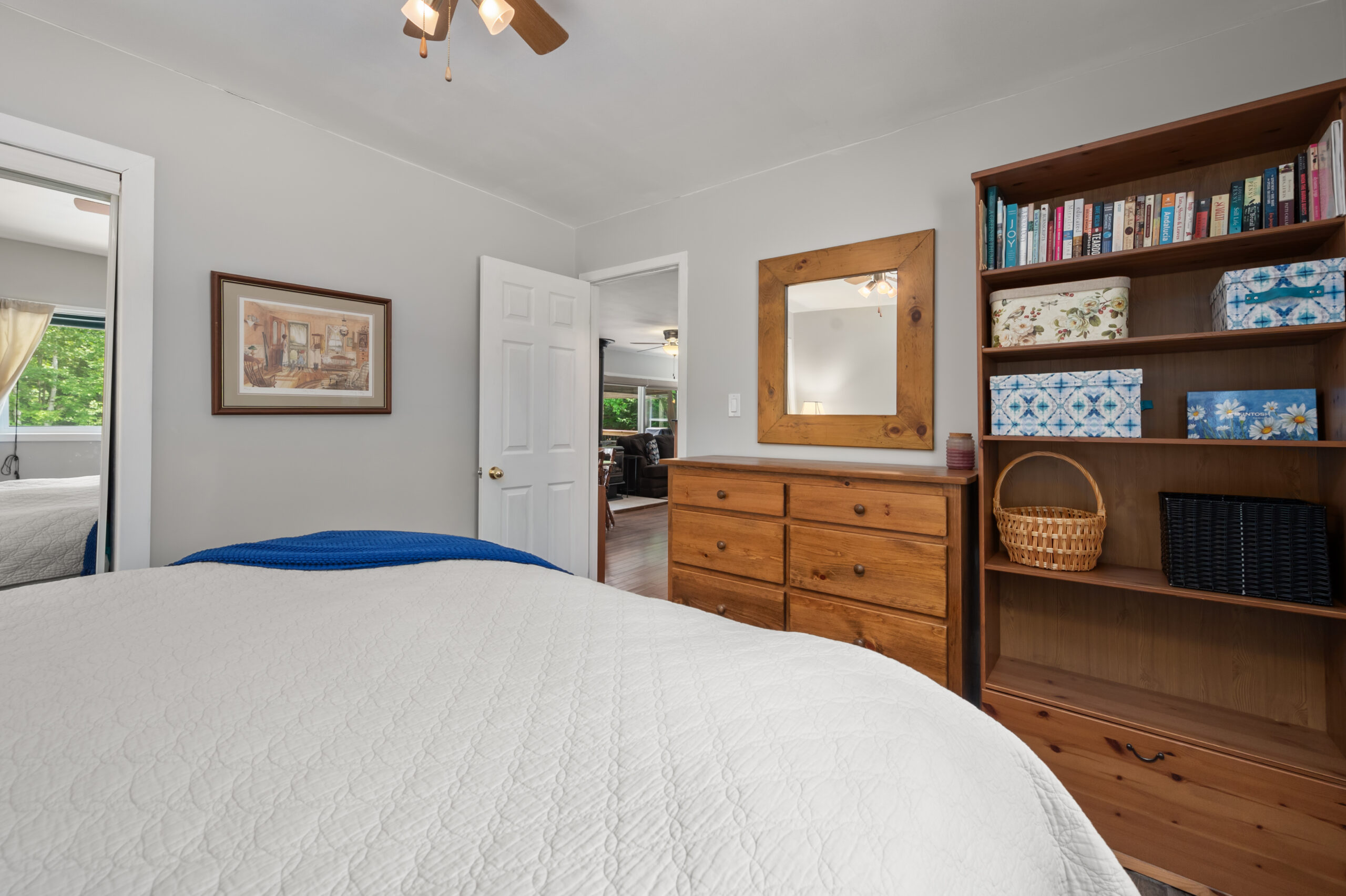 The end of a white bed faces a brown dresser and mirror