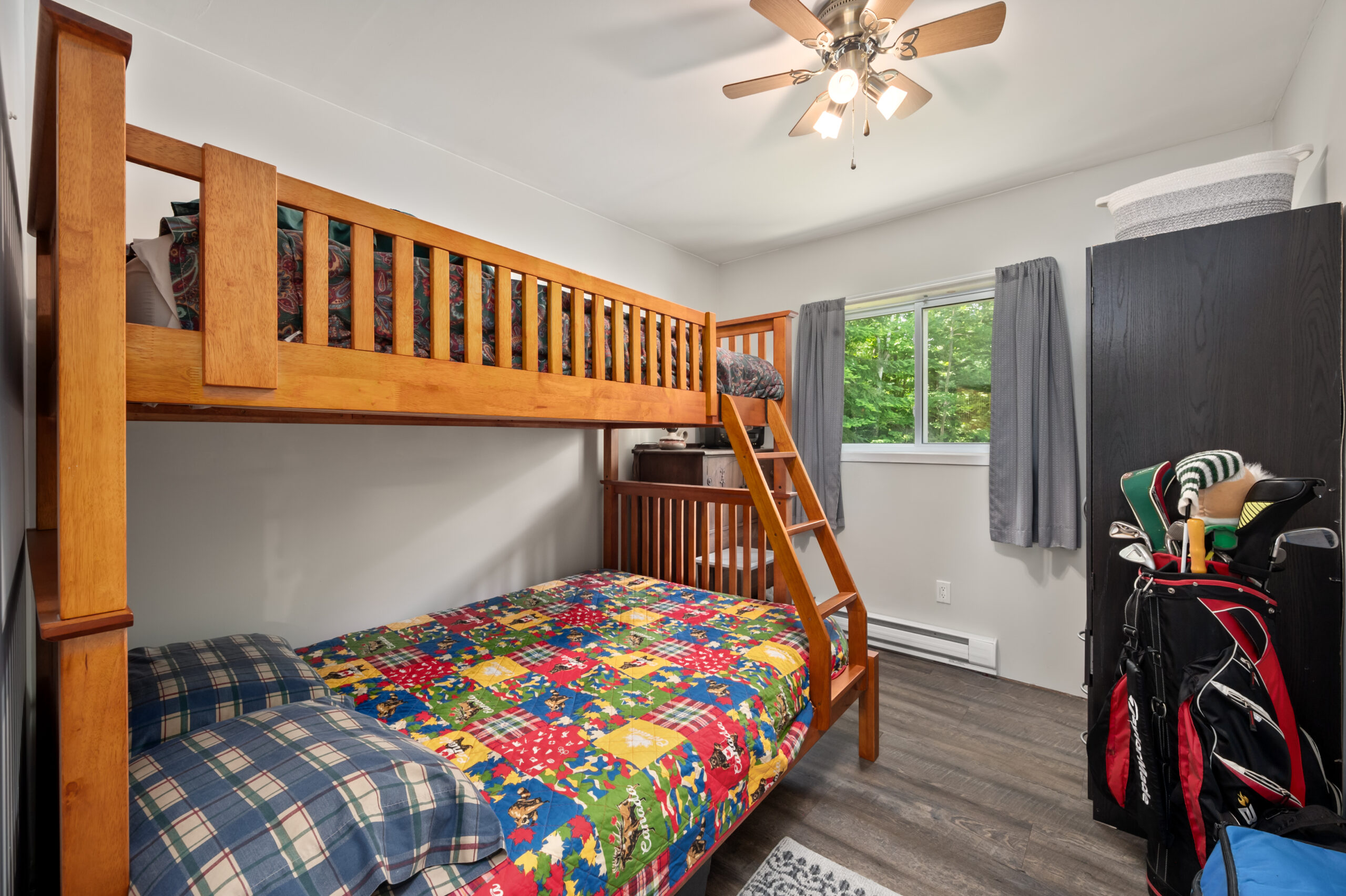 A wood bunk bed along the side of a bedroom. On one endd, a large window with grey curtains