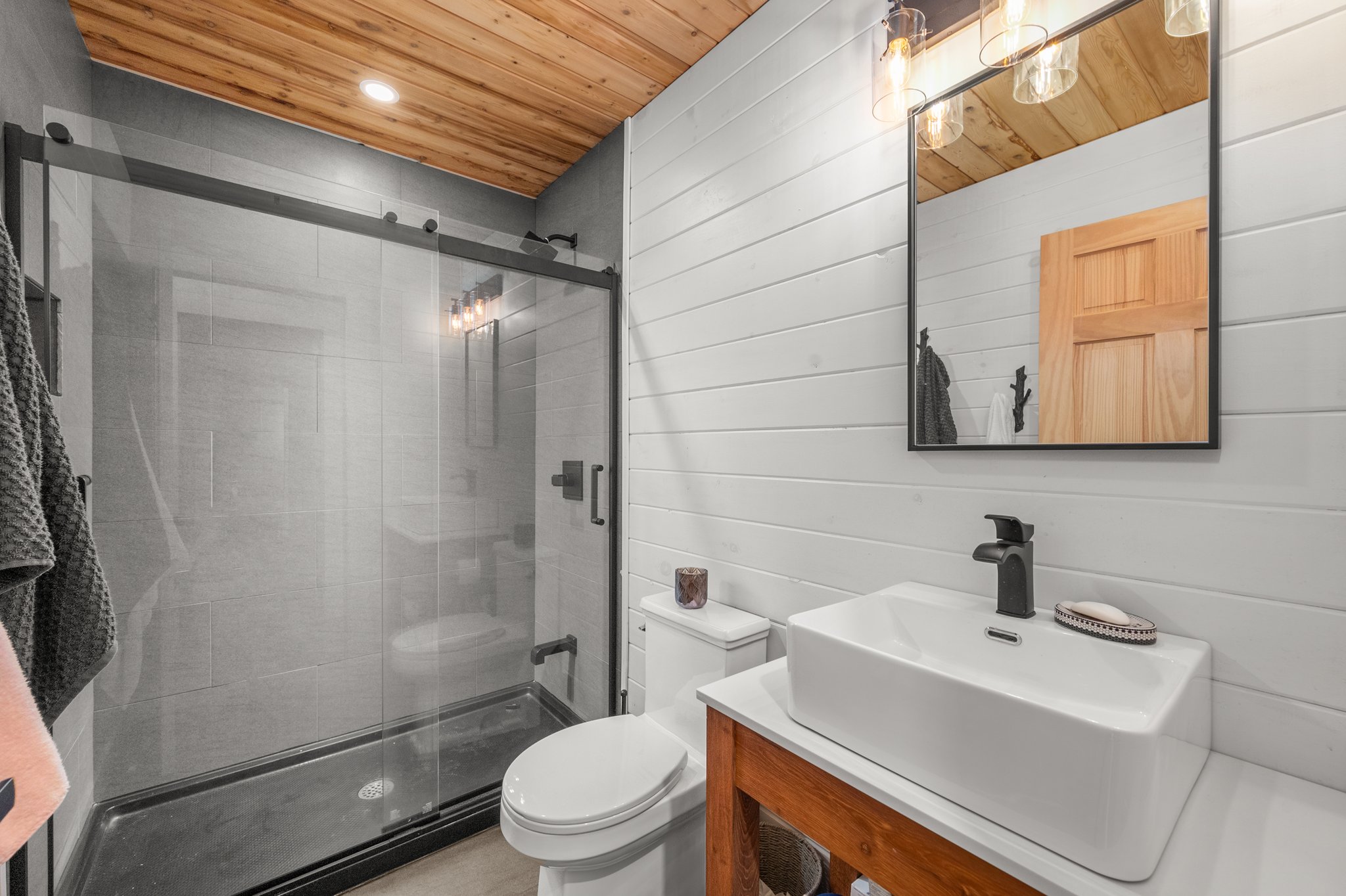 A glass shower beside a white toilet and a wood vanity