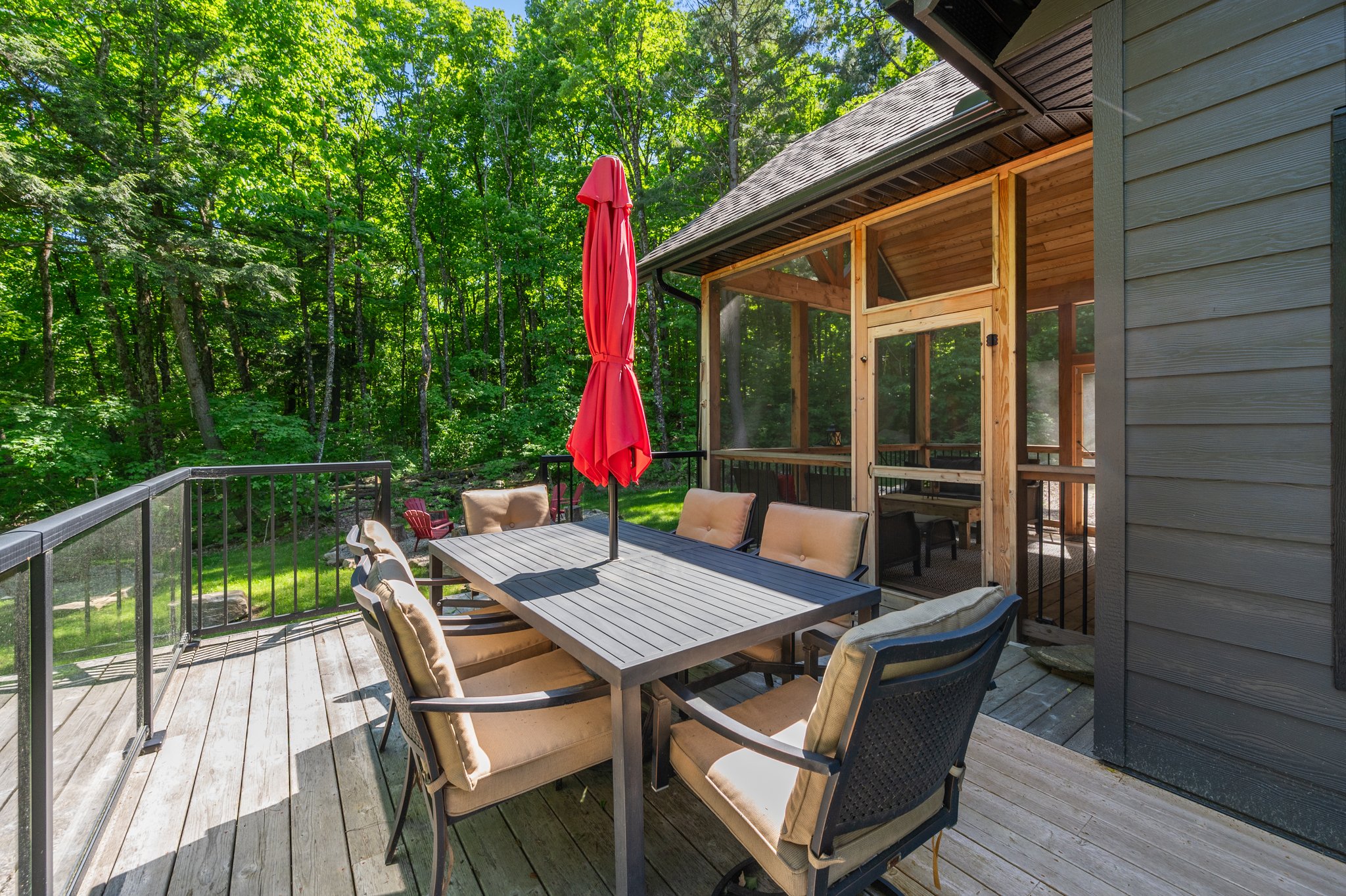 An outdoor dining table with a closed red umbrella and brown chairs on a deck