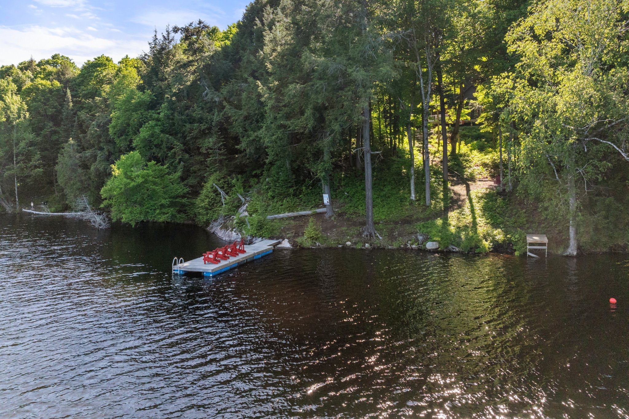 A long dock on the lake with red Muskoka chairs